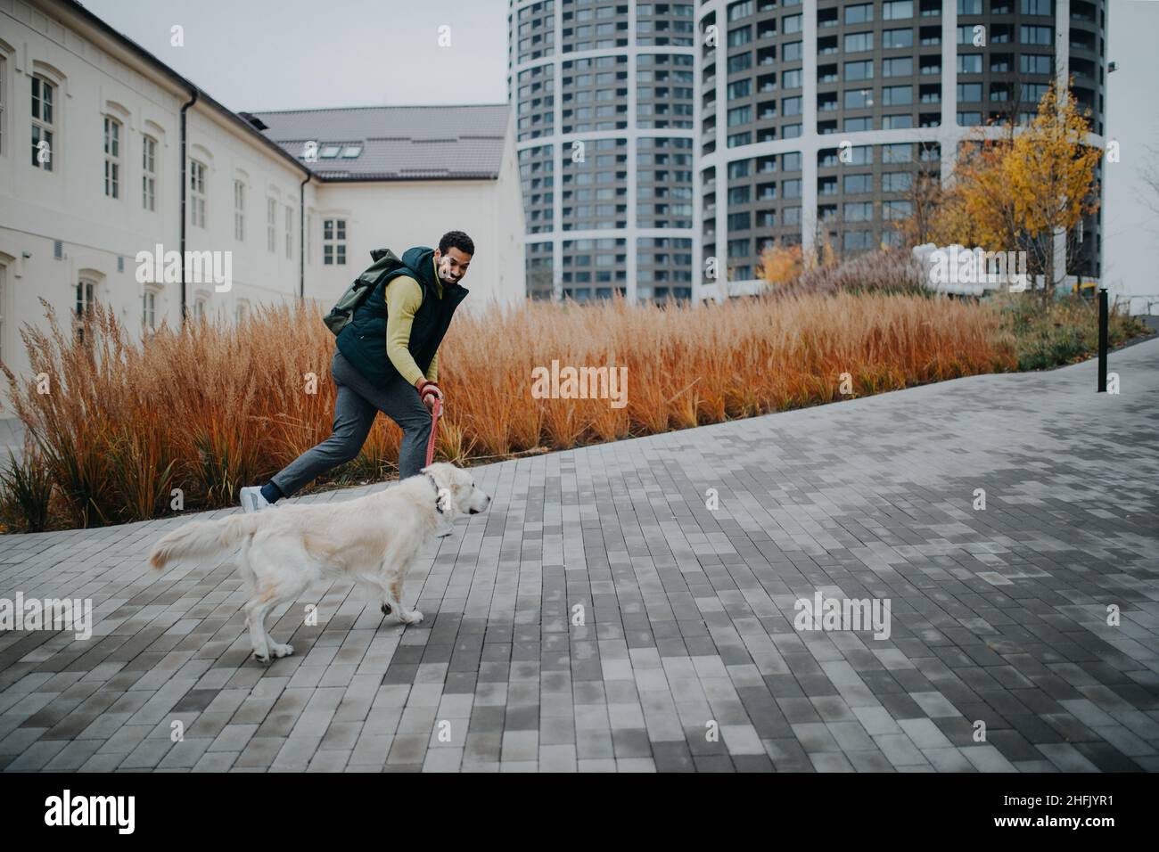 Glücklicher junger Mann, der mit seinem Hund an der Leine draußen in der Stadt läuft. Stockfoto