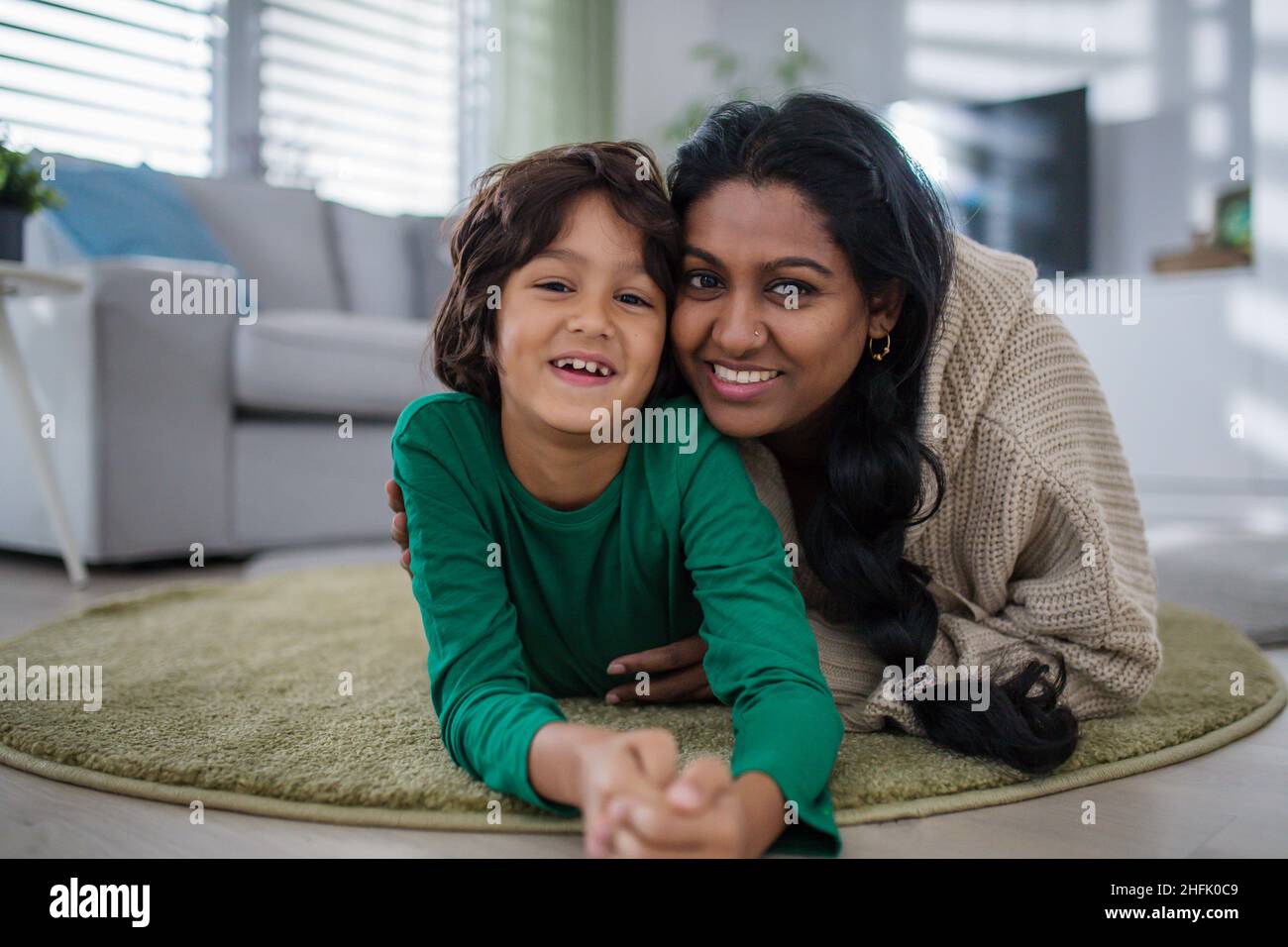 Indische Mutter, die mit ihrem kleinen Sohn zu Hause auf dem Boden liegt und die Kamera anschaut. Stockfoto