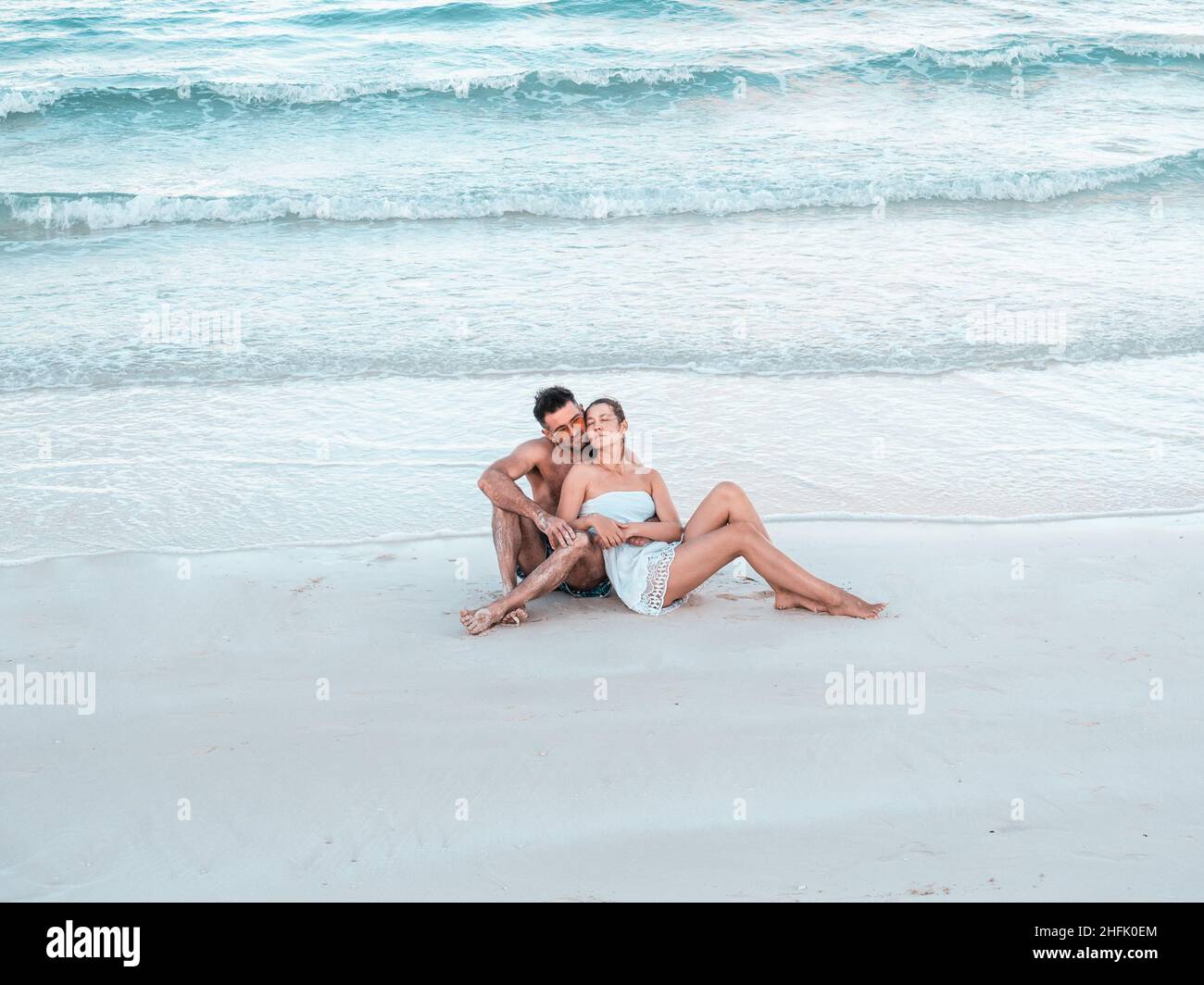 Schöner Mann und hübsche Frau sitzen am Strand Stockfoto