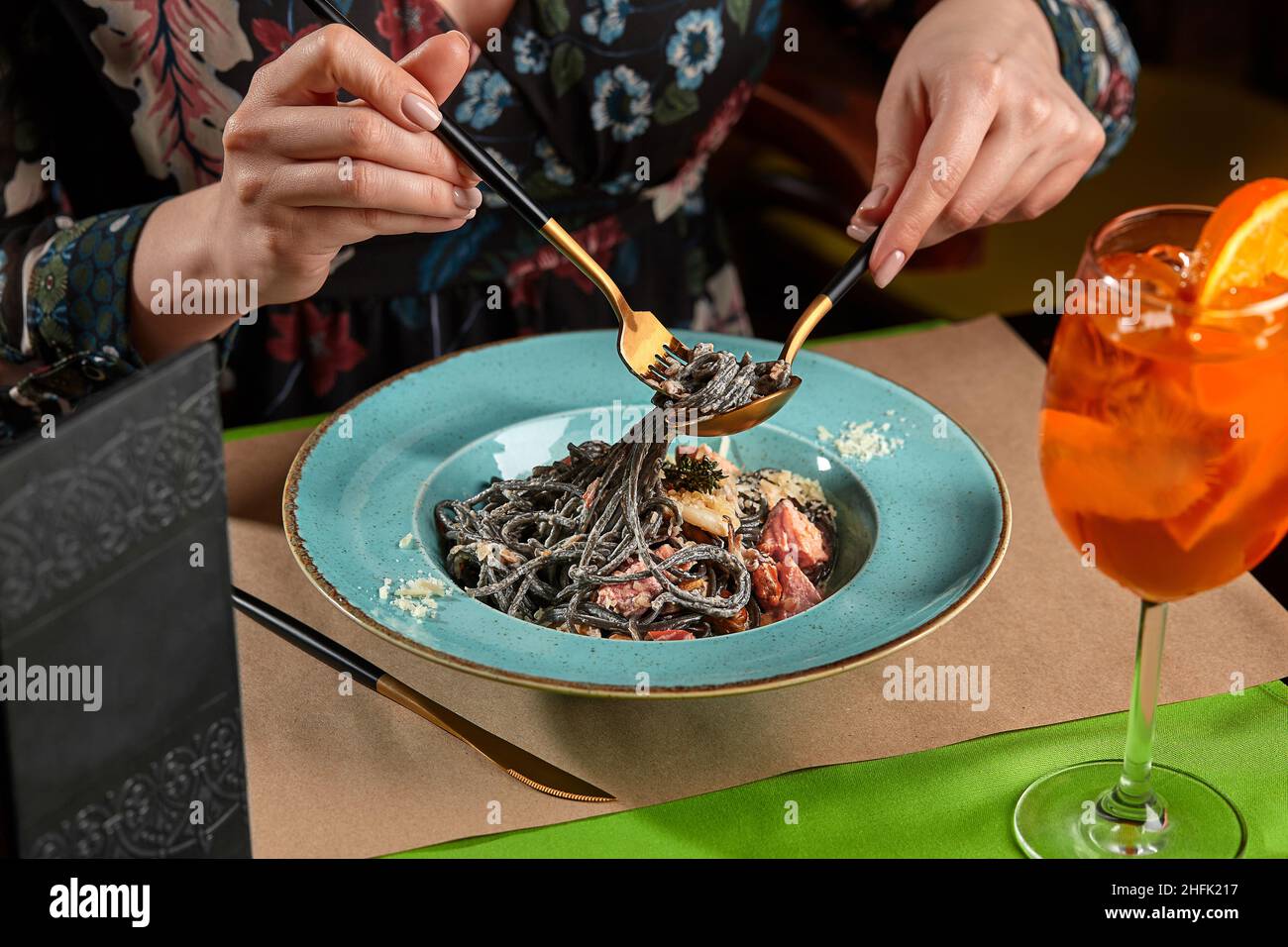 Eine kurze Aufnahme einer Frau, die schwarze Pasta mit Meeresfrüchten und Orangenspritz isst Stockfoto