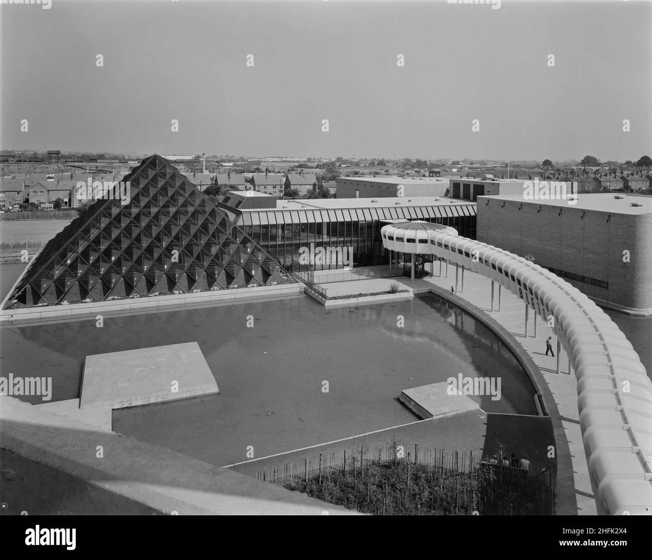 Bletchley Leisure Centre, Bletchley, Bletchley and Fenny Stratford, Milton Keynes, 30/07/1975. Eine erhöhte Aussicht auf das Bletchley Leisure Center aus dem Südwesten, mit Blick auf den See mit Bootstouren, das Schwimmbad, den Eingangsbereich und den erhöhten überdachten Eingangsbereich. Im Jahr 1971 kündigte Laing an, dass sie ein Freizeitzentrum in Bletchley für den Stadtbezirksrat von Bletchley errichten würden, um ein Freibad zu ersetzen. Weitere Verträge umfassten Phase II und Phase III und umfassten einen Swimmingpool, Squashplätze, einen See für Bootstouren und Nebenarbeiten. Der Komplex wurde 1974 fertiggestellt. Ein neues Freizeitzentrum war Stockfoto