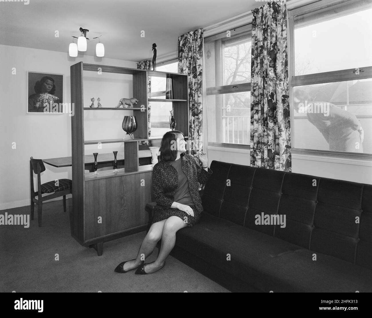 Bearwood House, Bearwood Road, Smethwick, Sandwell, 02/02/1966. Eine junge Frau, die im Lounge-Diner einer Wohnung im Bearwood House sitzt und draußen zu einem Freund winkt. „Sectra“ war ein französisches Stahlschalungskonzept für Wohnungen, an dem John Laing und Son Ltd 1962 die britischen Rechte erworben haben. Es handelte sich um eine Methode zur Verwendung von präzisionsgefertigten Stahlschalungen für die Platzierung von Strukturbeton in „Tunnelabschnitten“ in Raumteilbreiten und Deckenhöhen. Die Einheiten wurden in Reihen auf speziellen Schienen verschraubt, wobei der Beton in einem Arbeitsgang zu Wänden und Böden gegossen wurde. Die Schalung w Stockfoto