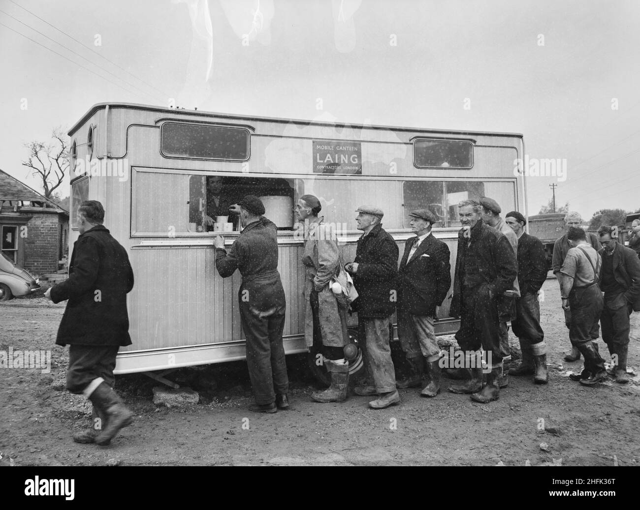 Fawley Reservoir, Fawley, New Forest, Hampshire, 08/10/1954. Mitarbeiter, die beim Bau des Fawley Reservoir beschäftigt waren, standen in einer mobilen Kantine Schlange. Im September 1954 begannen die Tiefbauarbeiten zur Bildung eines Reservoirs für die Esso Refinery Company in Fawley, Southampton. Der Vertragsort lag an der Spitze von Cadland Creek. Die Arbeiten beinhalteten das Dämmen des unteren Endes eines bestehenden Tals und den Bau eines Überlaufes, eines Stillbecken und eines Ausfalls. Stockfoto