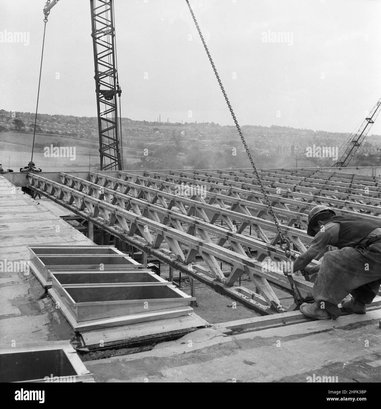 County High School, Gedling Road, Arnold, Gedling, Nottinghamshire, 12/09/1958. Zwei Arbeiter führen einen von einem Kran abgesenkten Laingspan-Balken während des Baus auf das Dach eines der Blöcke der Arnold County High School. Die Arbeiten auf dem Gelände begannen im März 1958 und die Bauarbeiten für das neue Schuljahr im September 1959 wurden abgeschlossen. „Laingspan“ war ein flexibles modulares System aus Rahmenkonstruktion, das aus vorgespannten Betonfertigteilen bestand. Laing entwickelte das System in Zusammenarbeit mit der Architects and Buildings Branch des Bildungsministeriums und dem beratenden Ingenieur AJ Stockfoto