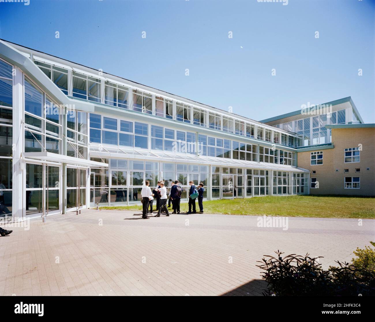 Durrington High School, The Boulevard, Worthing, West Sussex, 18/07/1996. Blick auf eine verglaste Verbindung zwischen Blöcken an der Durrington High School, mit einer Gruppe von Schulkindern draußen. Laing London und South East wurden Anfang 1990 &#X2019;s mit der Durchführung von Entwicklungsarbeiten an der Durrington High School für West Sussex County Council beauftragt. Phase I bestand aus drei neuen Blöcken, in denen wissenschaftliche Labors, Technologie-Workshops, Klassenzimmer, eine Bibliothek und andere Mitarbeiter- und Verwaltungsbereiche untergebracht waren. Phase II umfasste eine neue Sporthalle und einen Speisesaal. Weitere Arbeiten am Standort beinhaltete die Sanierung von Stockfoto