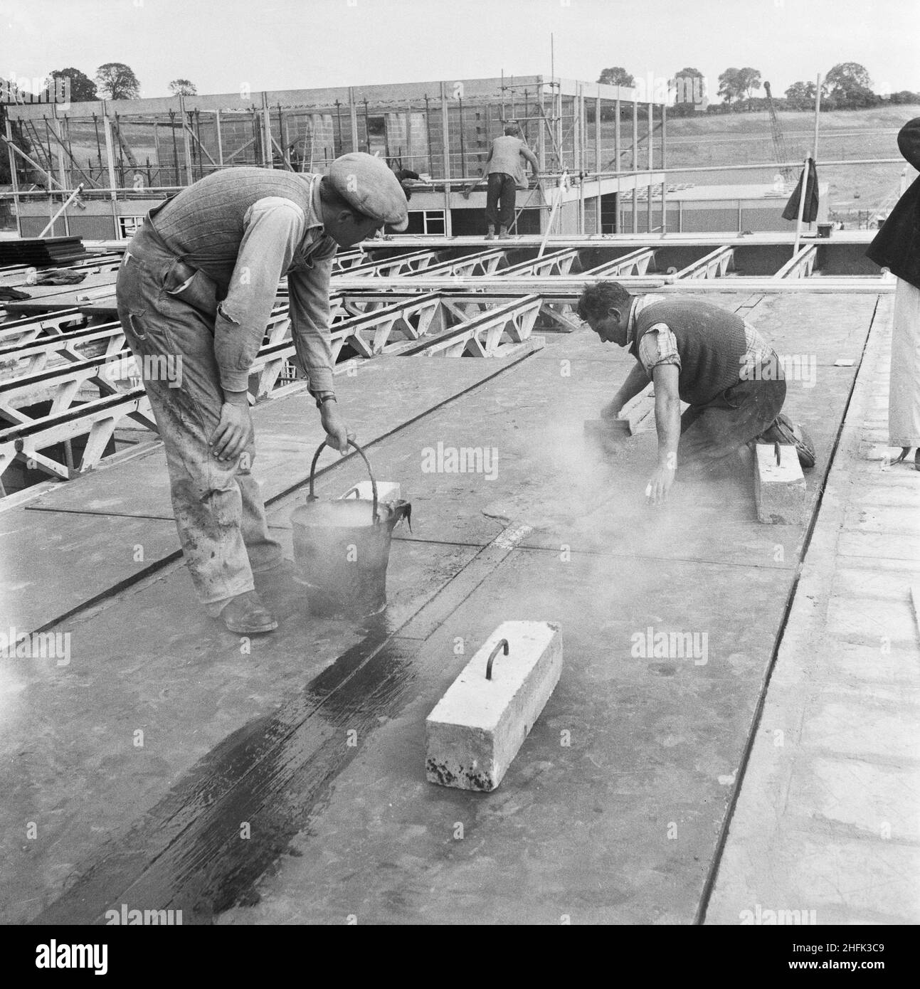 County High School, Gedling Road, Arnold, Gedling, Nottinghamshire, 12/09/1958. Zwei Arbeiter breiteten während des Baus der Arnold County High School heißen Teer aus, um die Fugen zwischen den Dachpaneelen zu versiegeln. Die Arbeiten auf dem Gelände begannen im März 1958 und die Bauarbeiten für das neue Schuljahr im September 1959 wurden abgeschlossen. „Laingspan“ war ein flexibles modulares System aus Rahmenkonstruktion, das aus vorgespannten Betonfertigteilen bestand. Laing entwickelte das System in Zusammenarbeit mit der Architects and Buildings Branch des Bildungsministeriums und dem beratenden Ingenieur AJ Harris. Die Arnold-Schule war die erste Stockfoto