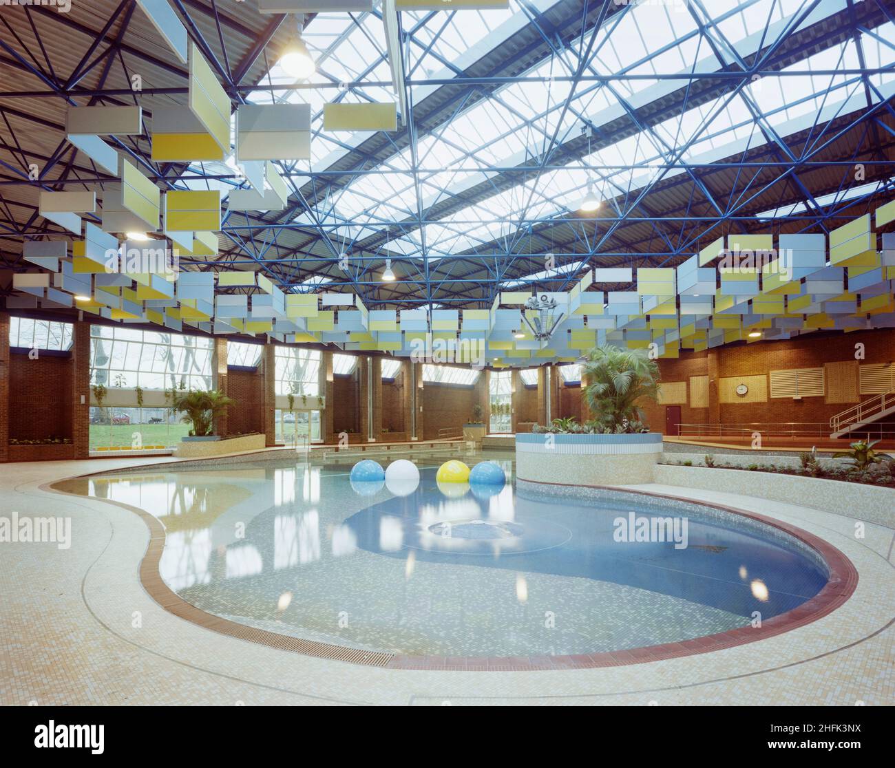 Kingfisher Leisure Centre, Fairfield Road, Kingston upon Thames, London, 30/11/1983. Die Strand- und Lagunenzonen des Swimmingpools im Kingfisher Leisure Centre, mit den schallabsorbierenden Schalldämmpaneelen, die von der Dachkonstruktion oben abgehängt sind. Im April 1982 wurde mit einer Zeremonie zum Rasenschnitt symbolisch mit dem Bau eines neuen Freizeitpools, Squash-Courts und einer Cafeteria in der Fairfield Road für den Royal Borough of Kingston upon Thames begonnen. Das Schema und die detaillierte Beschreibung wurden im Dezember 1981 von der Gemeinde vorgelegt. Die Hauptschwimmbad-Halle wurde entworfen, um eine Außenanlage zu erreichen Stockfoto