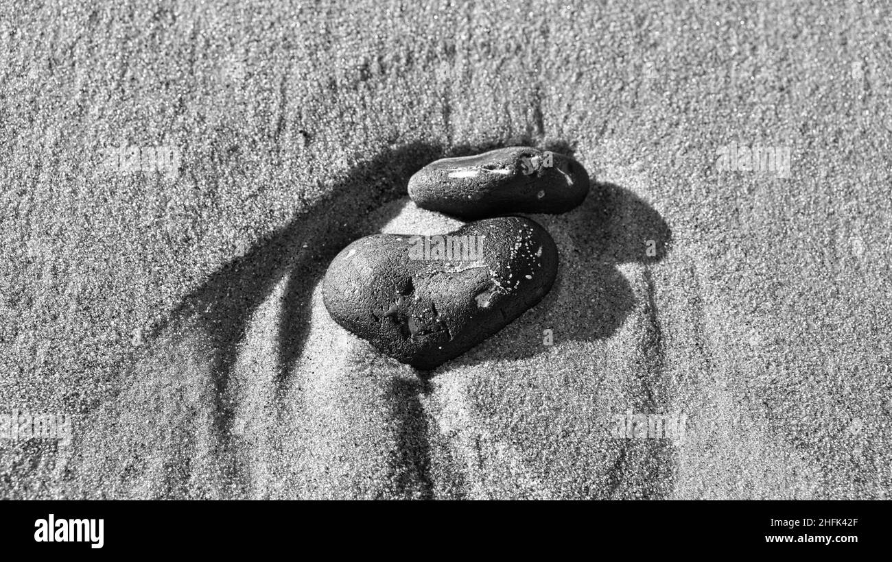 Herzförmiger Stein im Sand des Strandes an der OstseeA schwarz und weiß. Romantisches Symbol für verliebte Menschen. Kleines Zeichen als Stillleben. Stockfoto