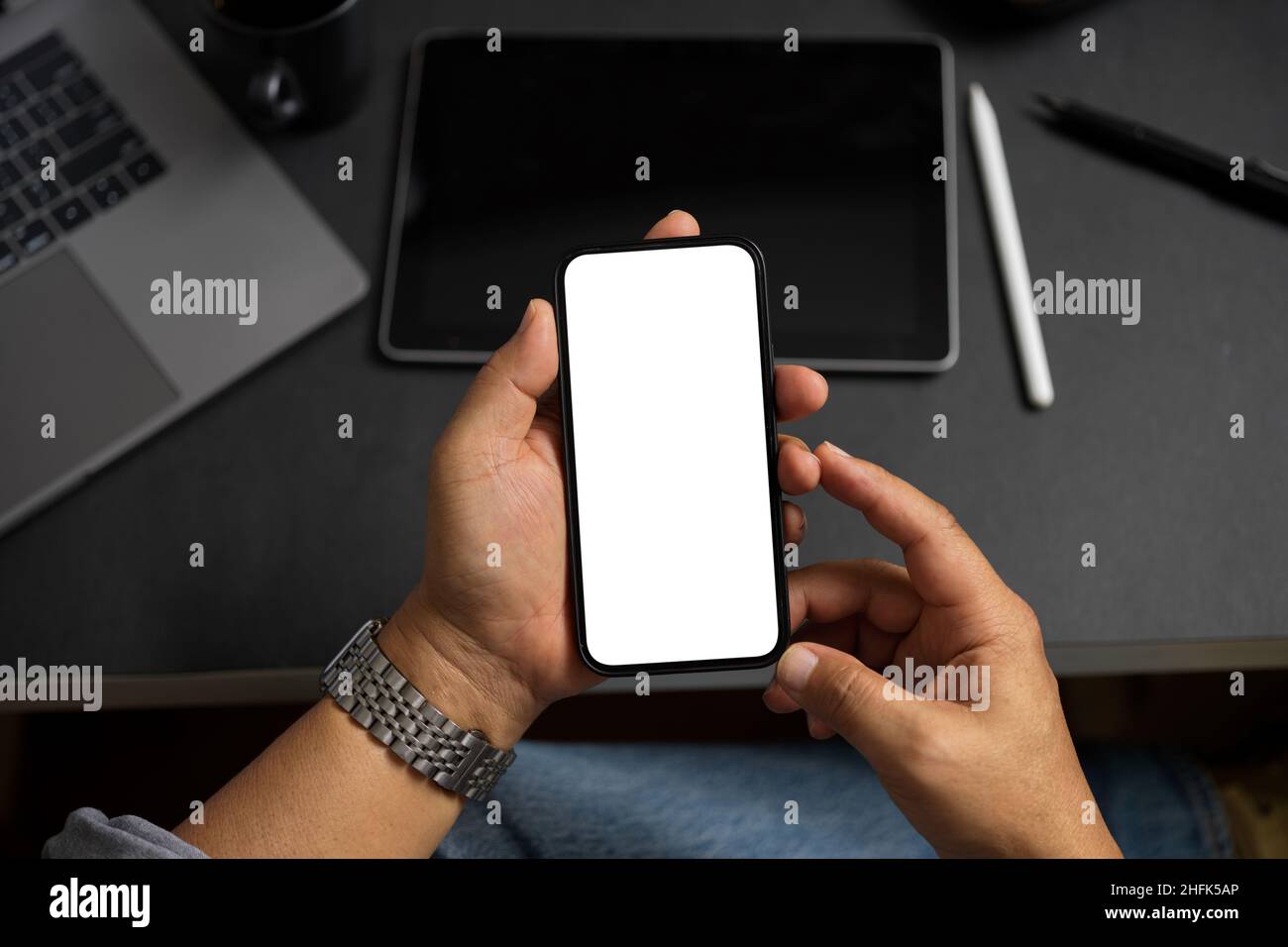 Mockup-Bildschirm eines modernen Smartphones in den Händen eines männlichen oder erwachsenen Mannes über einem Bürotisch. Nahaufnahme Stockfoto