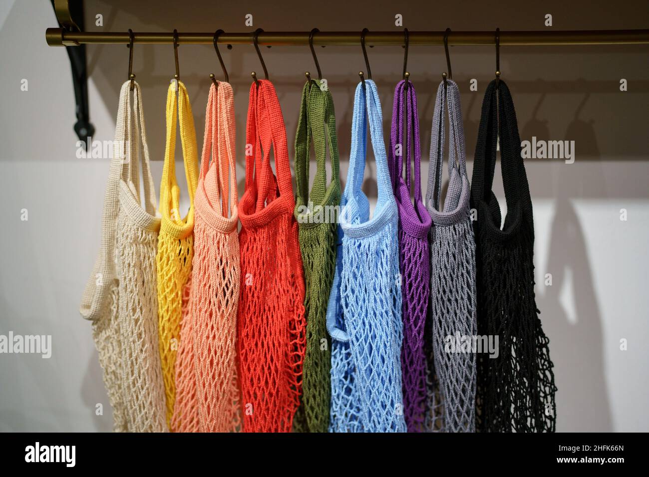 Bunte, umweltfreundliche Einkaufstaschen an Kleiderbügeln, mehrfarbige, gewebte Öko-Taschen aus Mesh Stockfoto