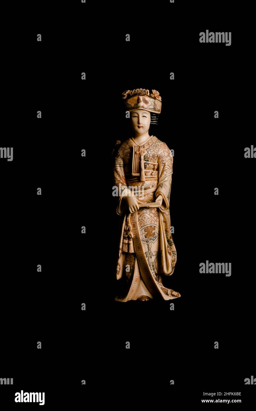 Alte Figur einer Geisha mit einem Fächer in den Händen aus Elfenbein auf schwarzem Hintergrund. Vertikales Bild. Stockfoto