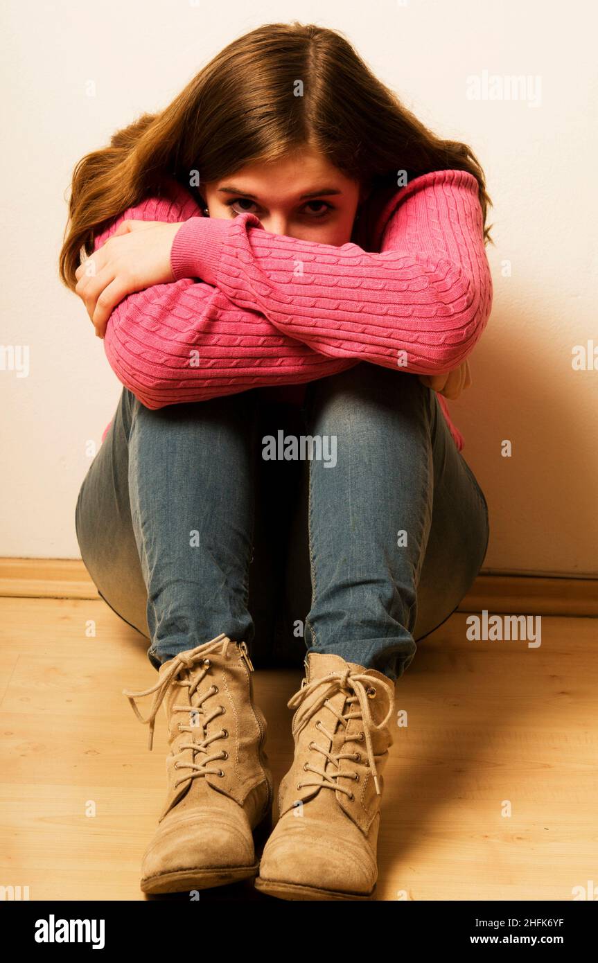 Junges Mädchen, das auf dem Boden sitzt, verängstigt oder Angst hat, ihr Gesicht zu verstecken Stockfoto