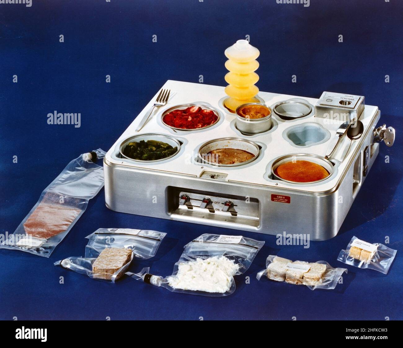 (1972) --- Eine Nahaufnahme eines Tabletts, das für das Skylab-Programm vorgesehen ist. Neben dem Tablett liegen mehrere Packungen mit Lebensmitteln aus dem Raum. Die Lebensmittel im Tablett sind verzehrfertig. Aus dem Tablett, beginnend von unten links: Traubengetränk, Rinderbraten, Huhn und Reis, Rindersandwiches und Zuckerplätzchenwürfel. Im Tablett, von hinten links: Orangengetränk, Erdbeeren, Spargel, Prime Rib, Essensrolle und Butterscotch-Pudding in der Mitte. Stockfoto
