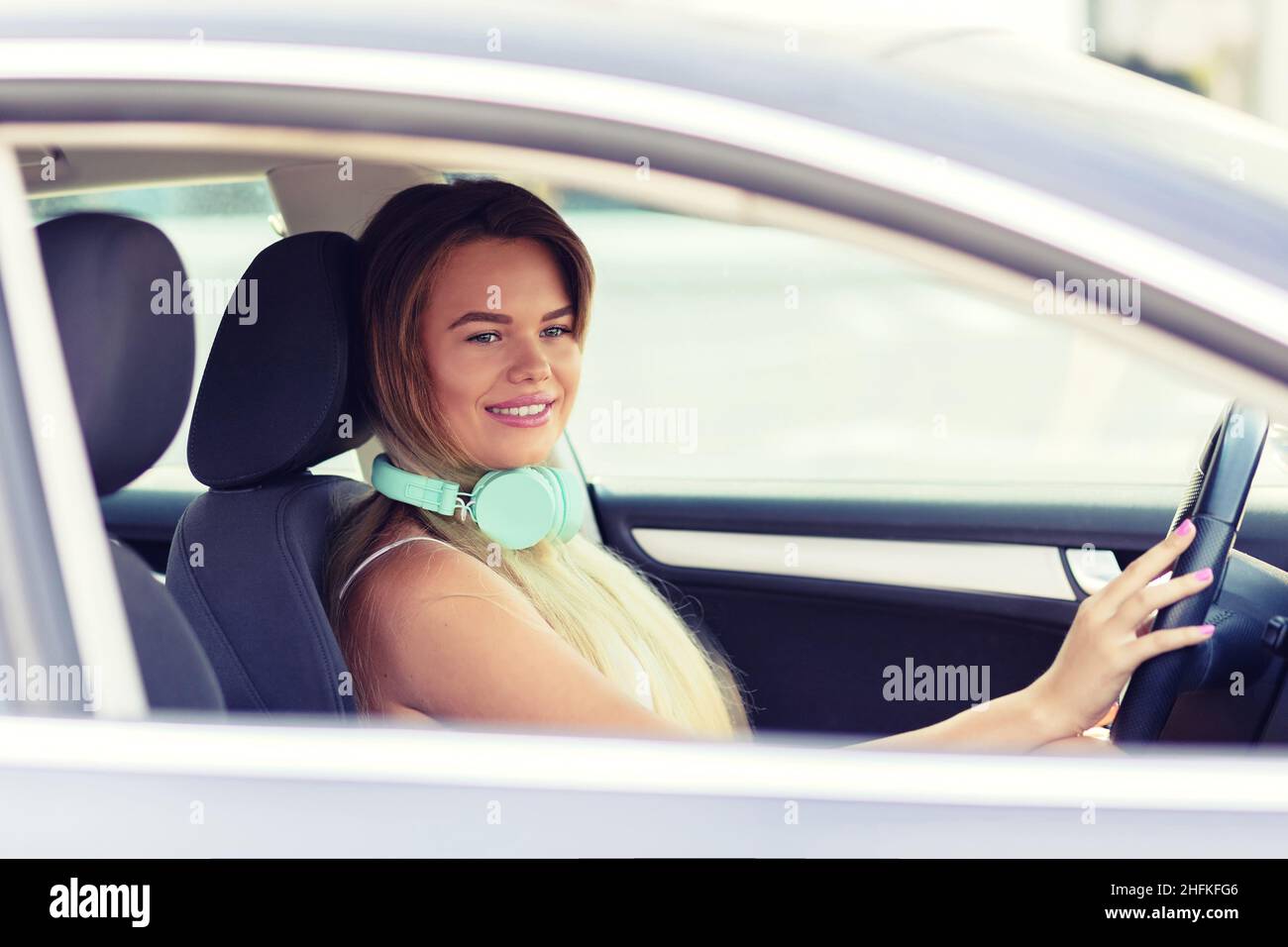 Schöne und modische junge Frau, die ihr neues Auto fährt, während sie Musik hört Stockfoto