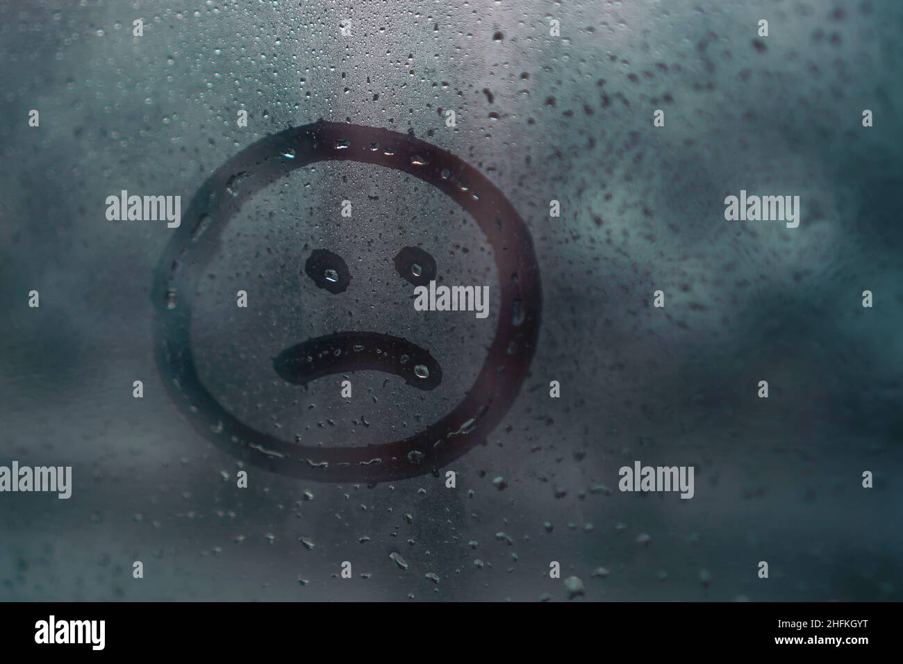 Trauriges Smiley, das von Hand auf nasses, beschlagenes Glas vom Regen gezeichnet wurde, kopiere den Raum. Konzept von Einsamkeit, Traurigkeit, schlechtem Wetter Stockfoto