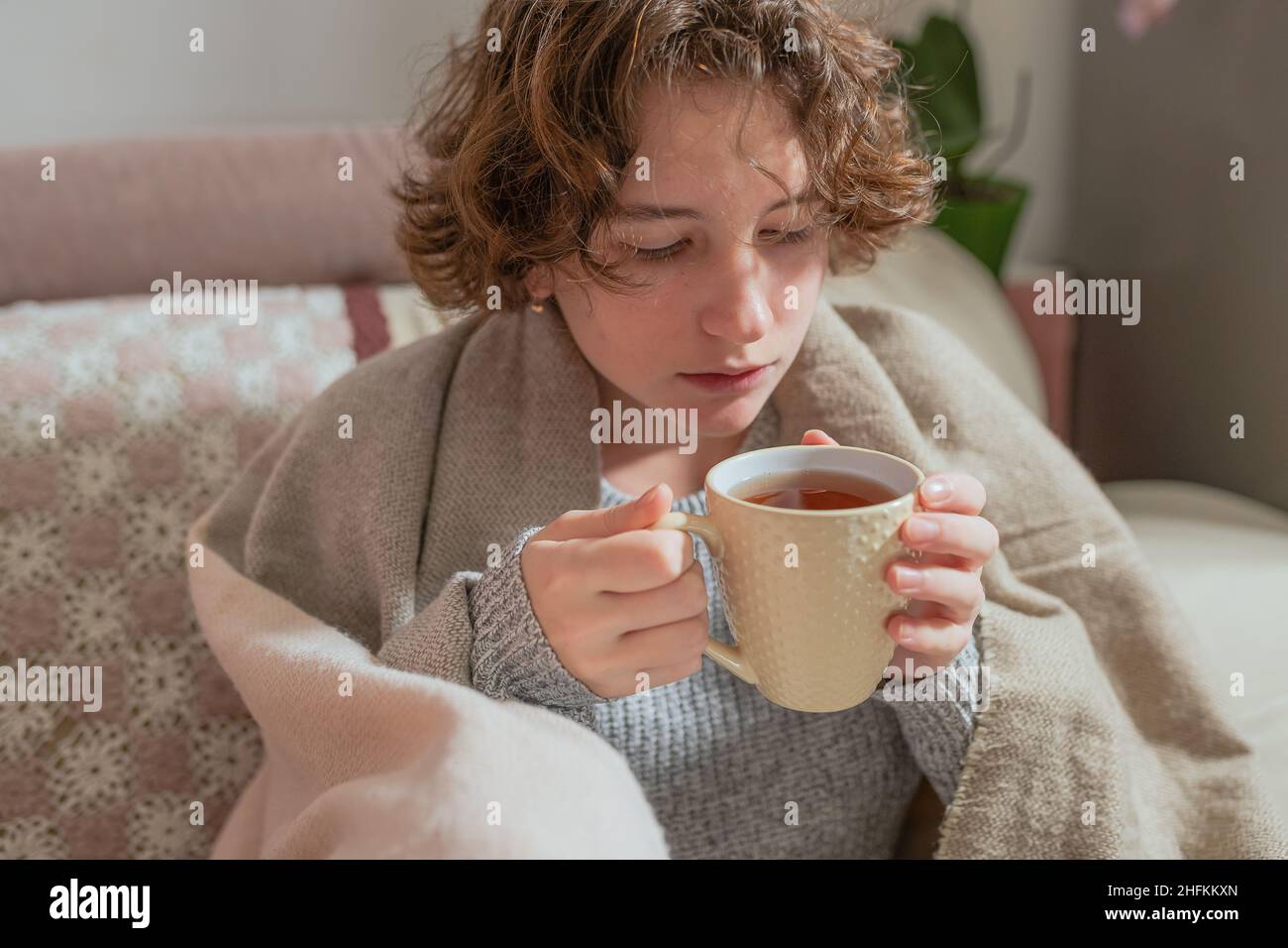 Gefrorene junge Frau in eine warme Decke eingewickelt trinken heißen Kräuter-Vitamin-Tee zu wärmen oder eine Erkältung zu behandeln Stockfoto
