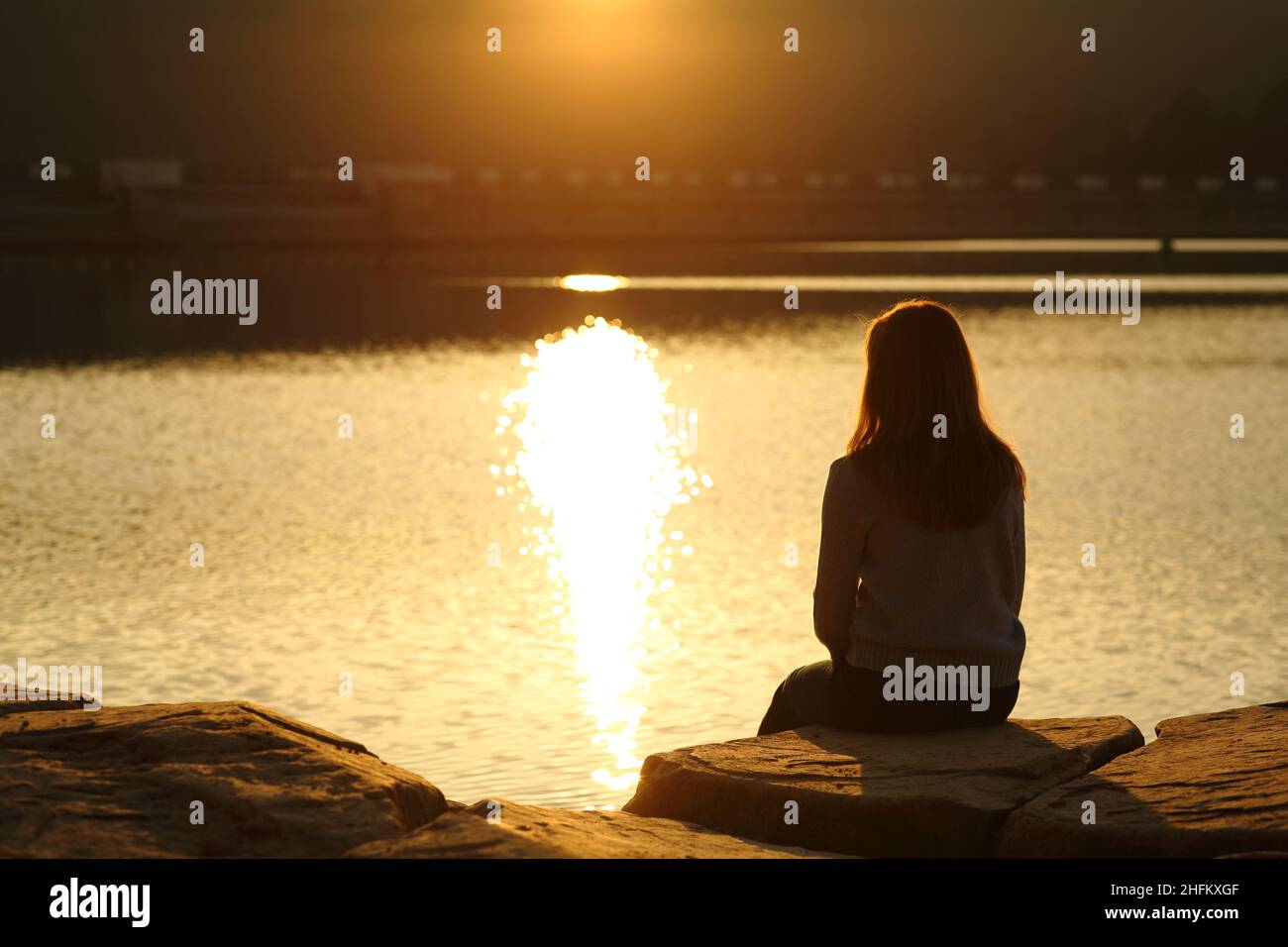 Rückansicht einer Frau Silhouette Betrachtung Sonnenuntergang in einem See Stockfoto