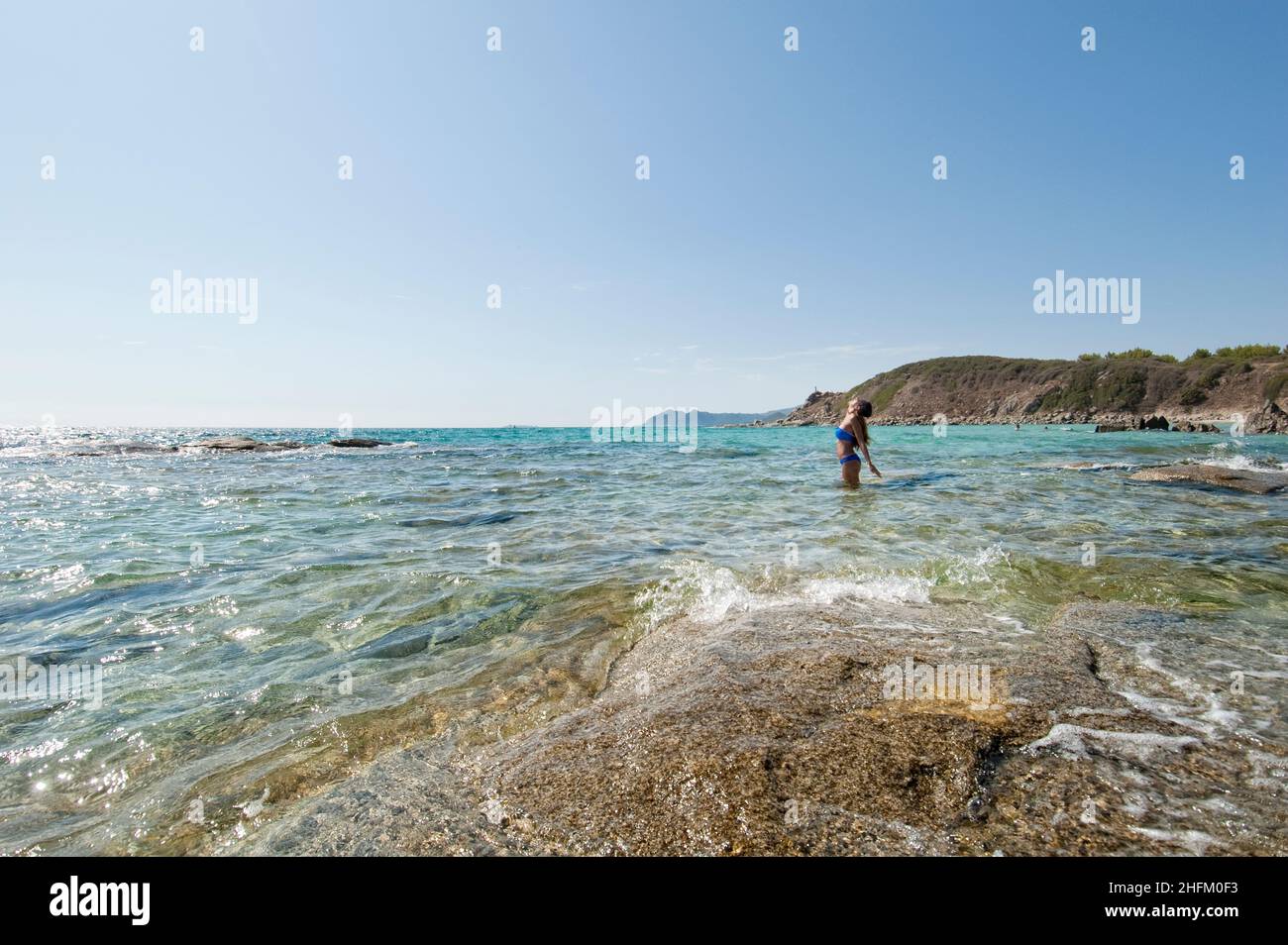 Junge schöne Frau, die auf Felsen im kristallklaren Wasser der Insel Sardinien steht. Stockfoto