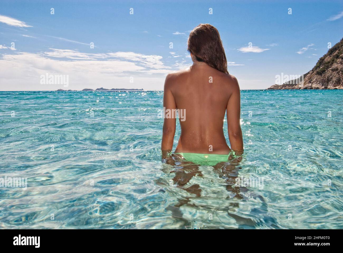 Junge Frau, die in den Horizont blickt und im kristallklaren Wasser auf Sardinien steht Stockfoto
