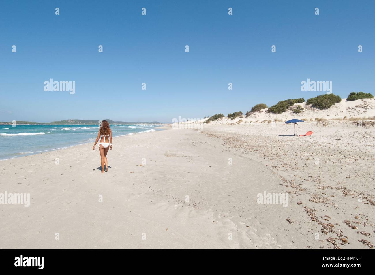 Junge Frau, die an einem weißen Sandstrand am Strand von Porto Pino auf Sardinien spazieren geht Stockfoto