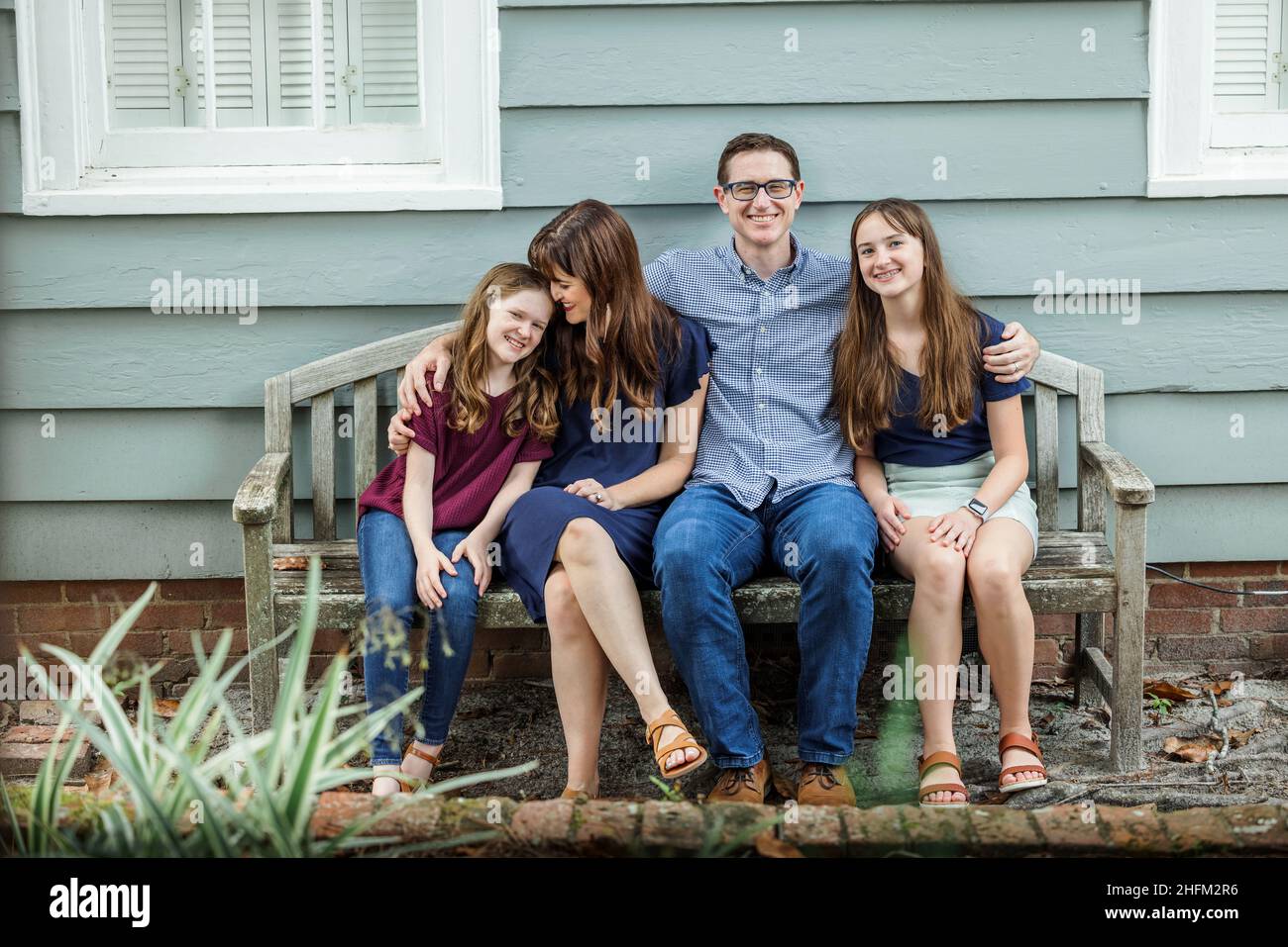 Eine Familie mit Mutter, Vater und zwei Töchtern, die draußen auf einer Bank sitzen Stockfoto