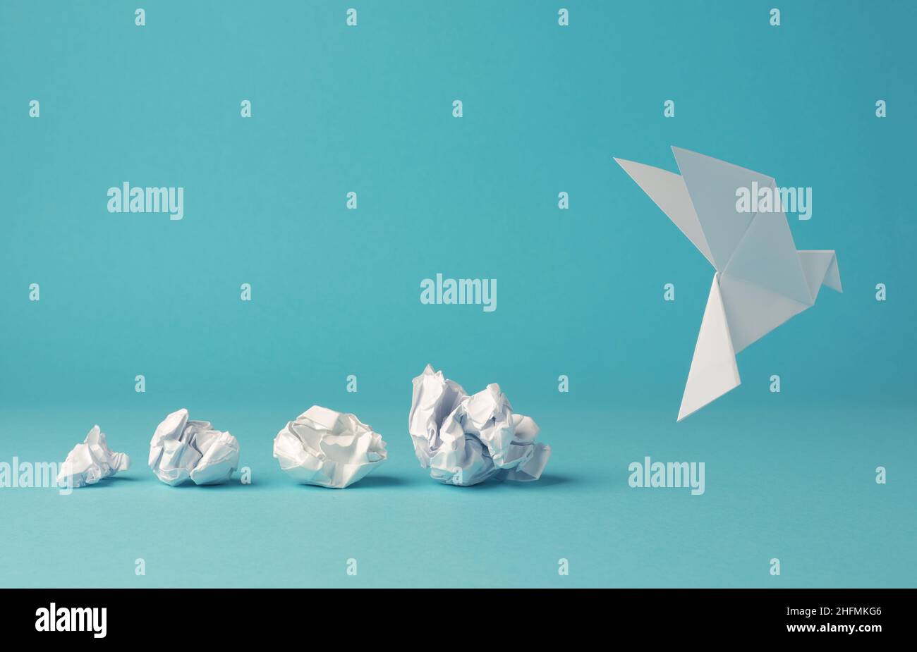 Zerknitterte Papierkugeln mit Origami-Papiertaube, Friedens-, Freiheit- oder Chancenkonzept auf blauem Hintergrund Stockfoto