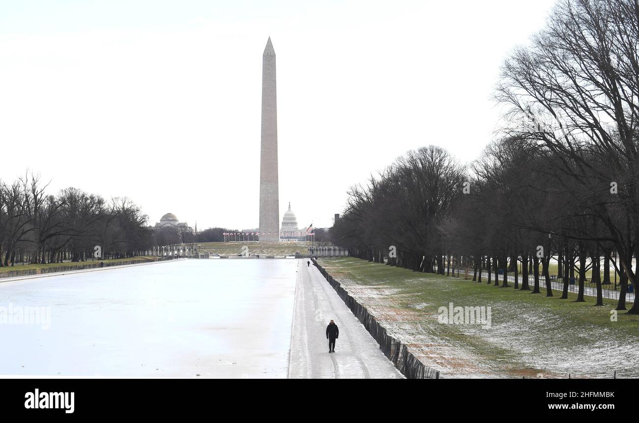 Nach einer stürmischen Nacht in Washington, USA, 17. Januar 2022, geht eine Person entlang des gefrorenen Lincoln Memorial Reflecting Pools mit dem Washington Monument und dem US Capitol im Hintergrund. REUTERS/Mike Theiler Stockfoto
