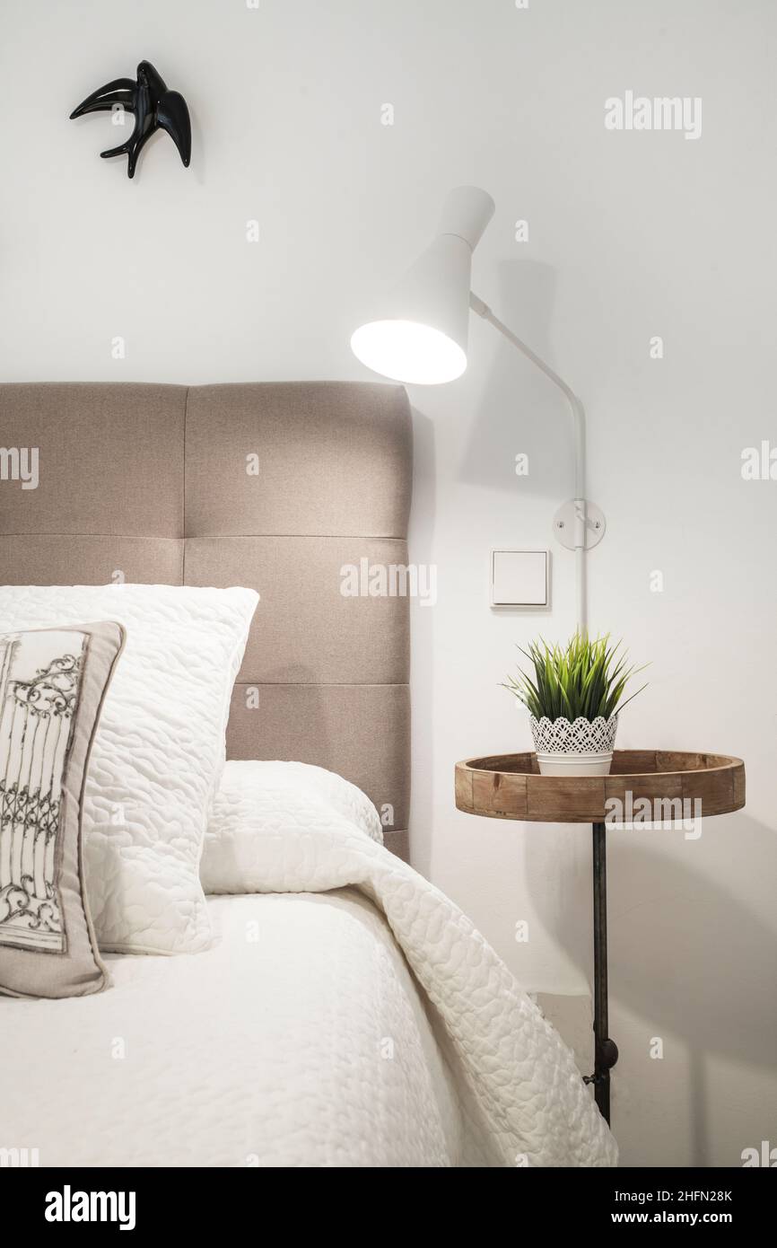 Gepolstertes Kopfteil in einem Schlafzimmer mit weißer Lampe und runder Nachttisch aus Holz Stockfoto