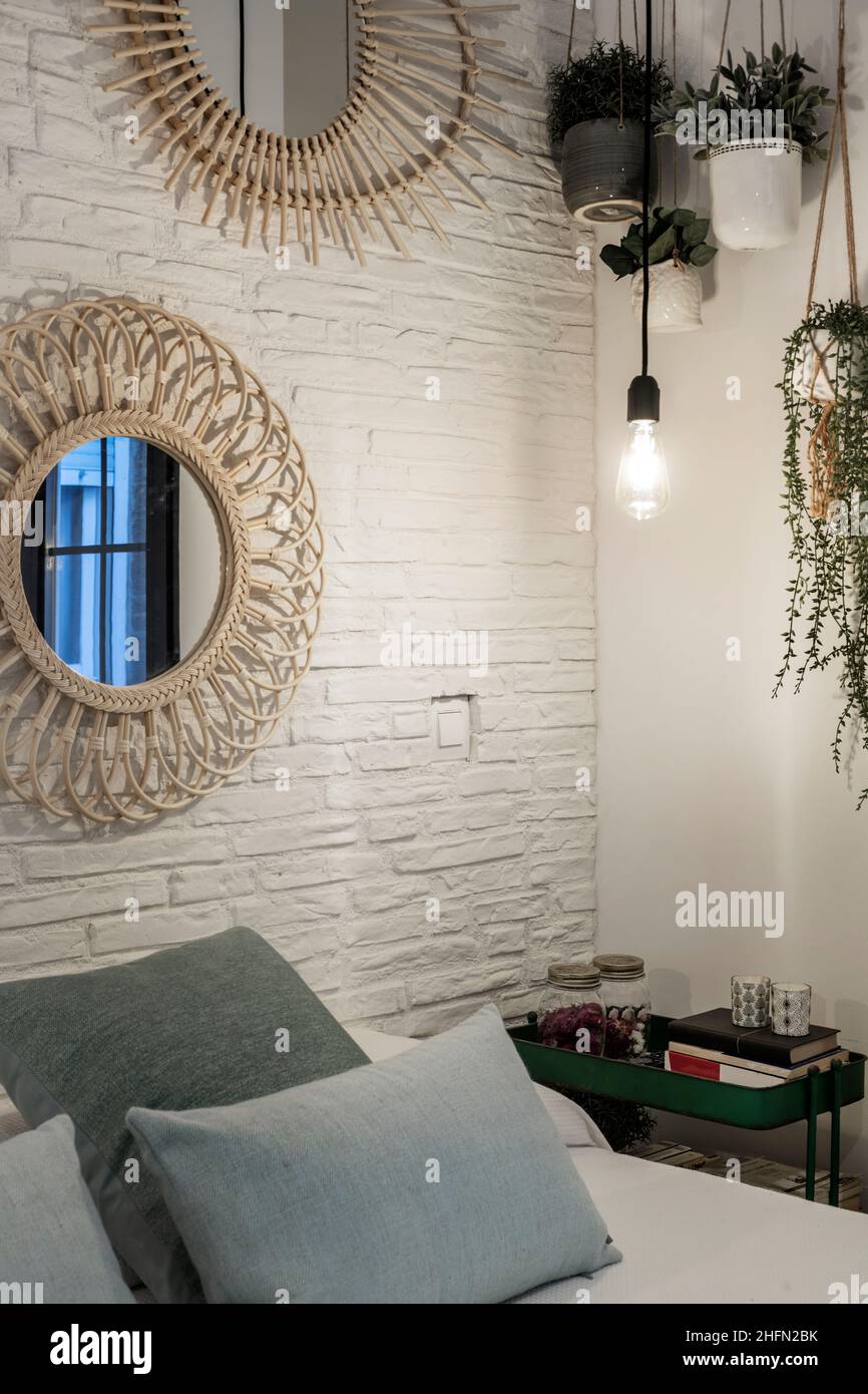 Ecke eines Schlafzimmers mit einer weißen Ziegelwand, hängenden Pflanzen und Kissen auf dem Kopfteil Stockfoto