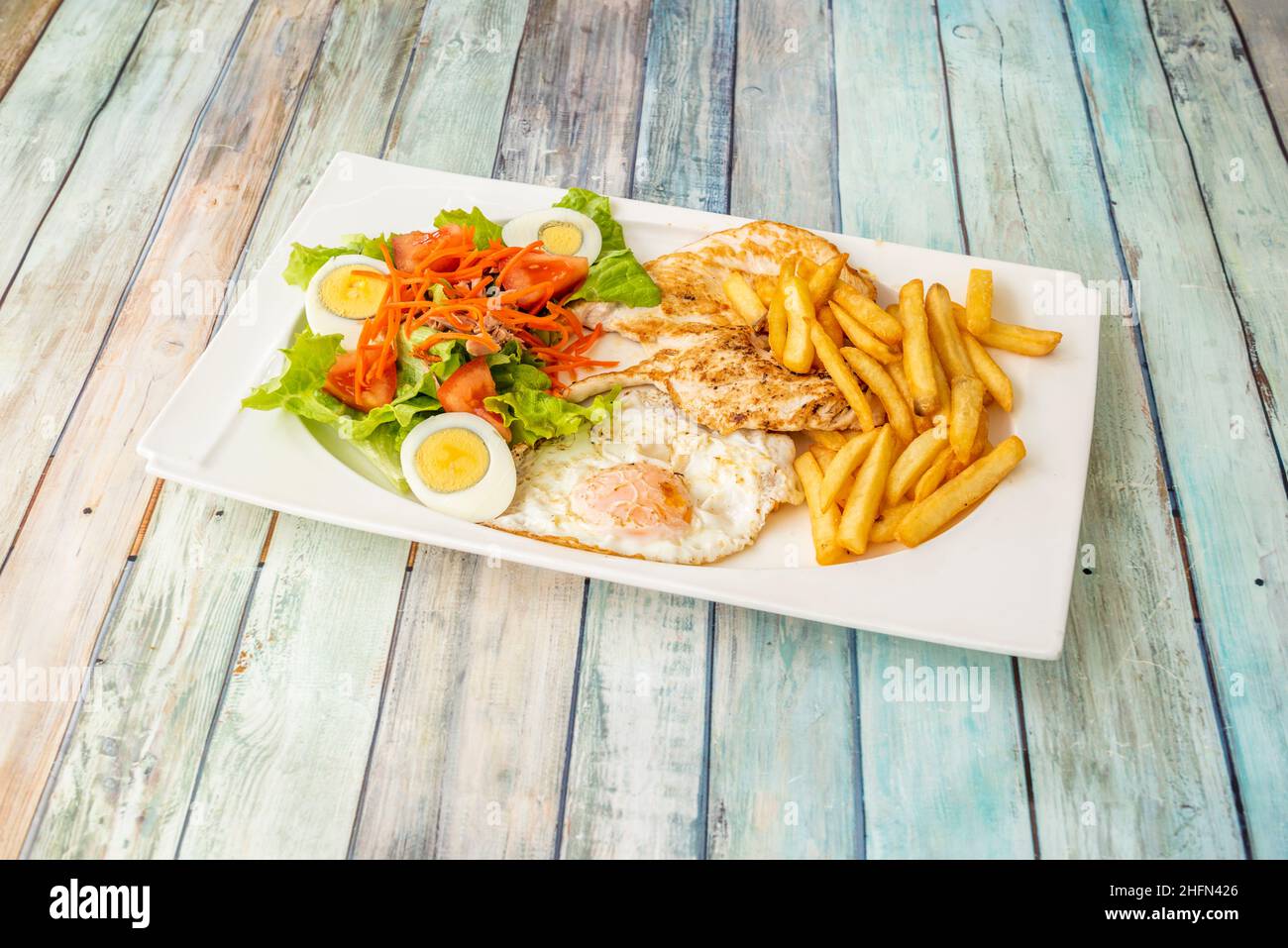 Gesunder Kombi-Teller mit pommes frites, gegrilltem Hähnchenfilet und einem gebratenen und einem in Scheiben geschnittenen Ei, das mit Salat und Karotten gekocht wird Stockfoto