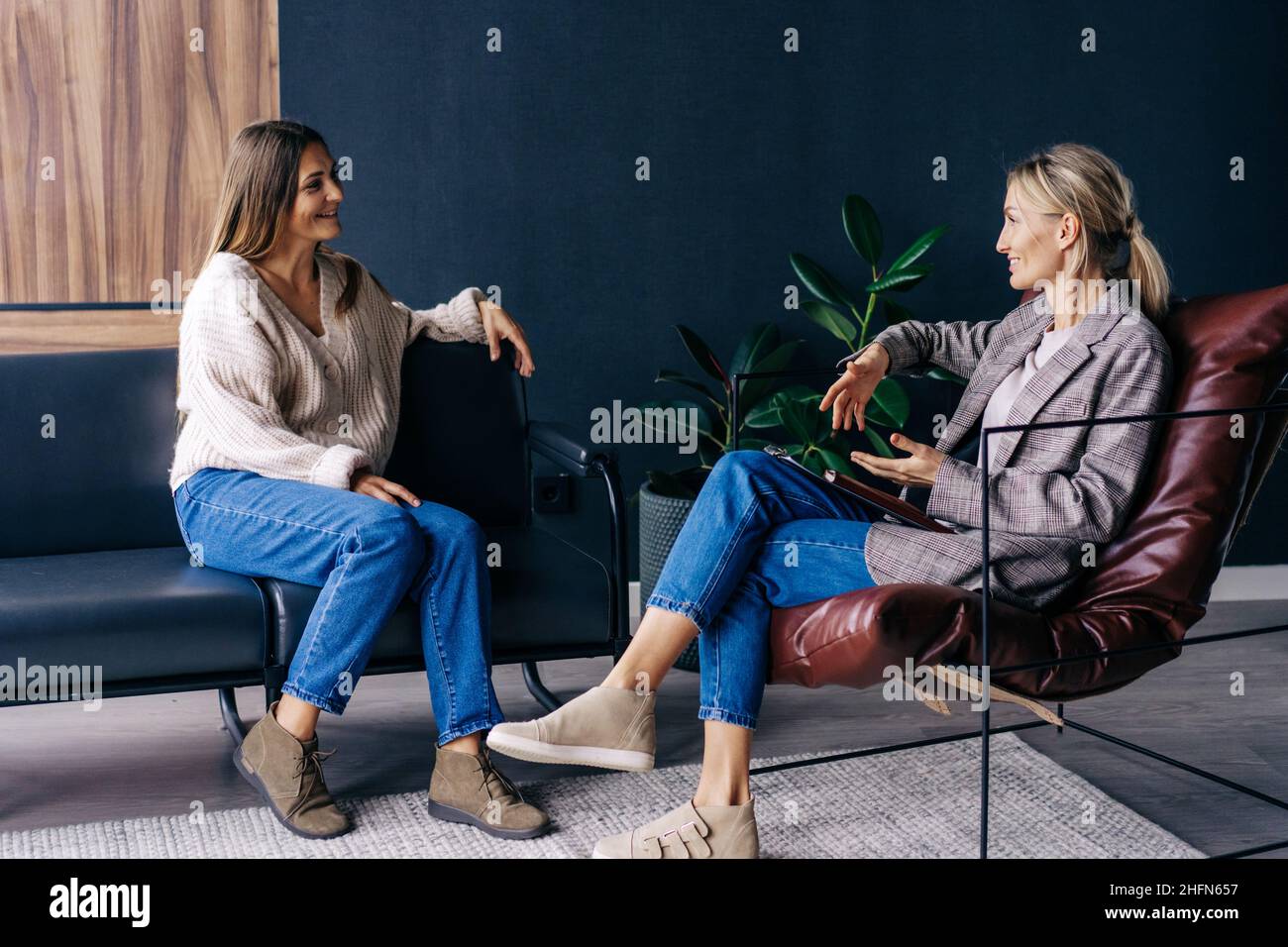 Zwei moderne, stilvolle Frauen sitzen im Büro und diskutieren über Ideen und die Umsetzung von Plänen. Stockfoto