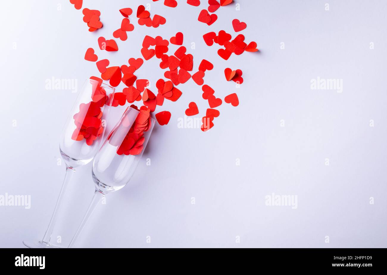 Sektflöten mit roten Herzformen, die durch den Kopierraum auf weißem Hintergrund verstreut sind Stockfoto