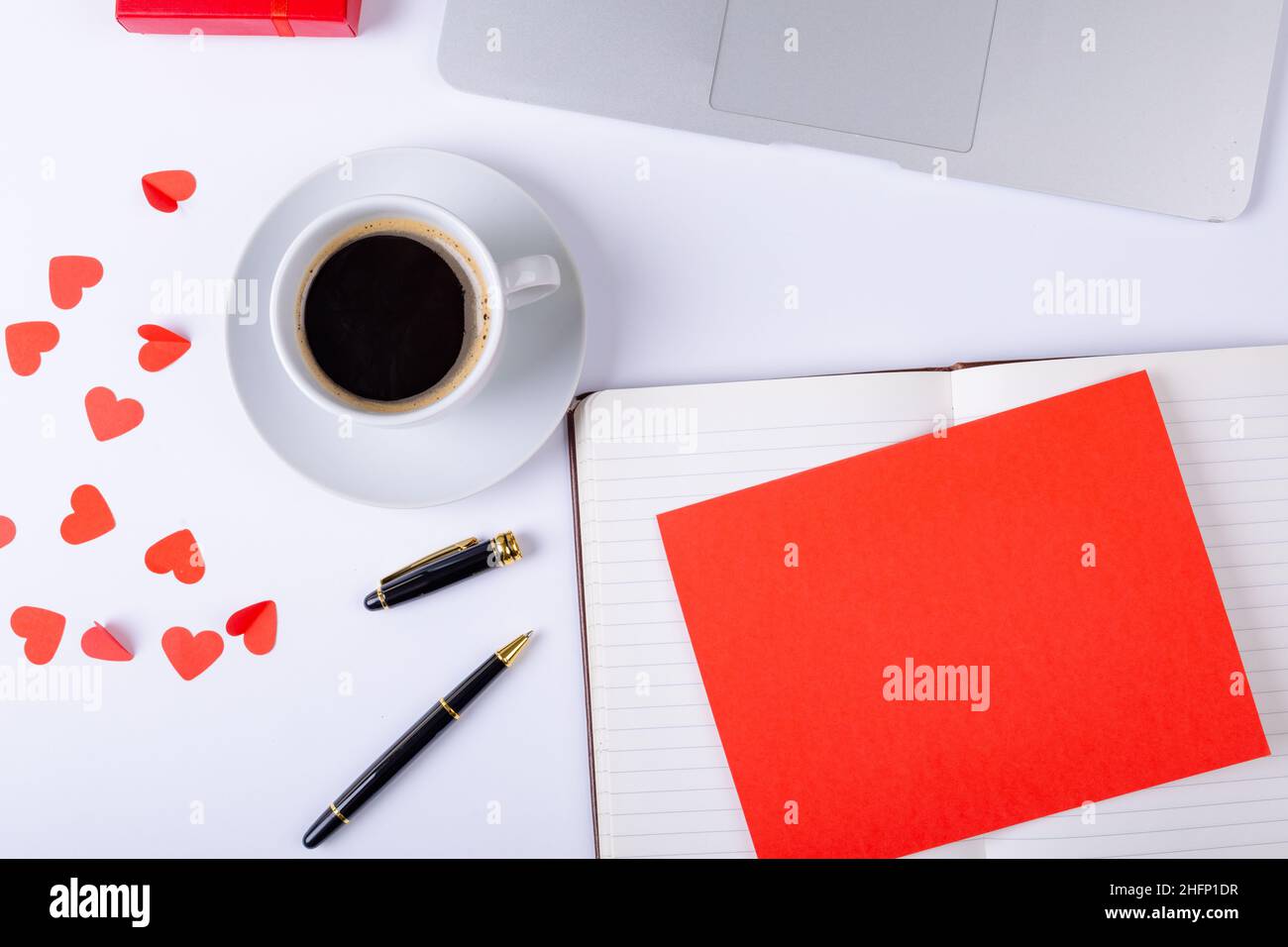 Leeres rotes Papier auf offenem Tagebuch mit Platz für Kopien bei Kaffee und Herzform am Schreibtisch Stockfoto