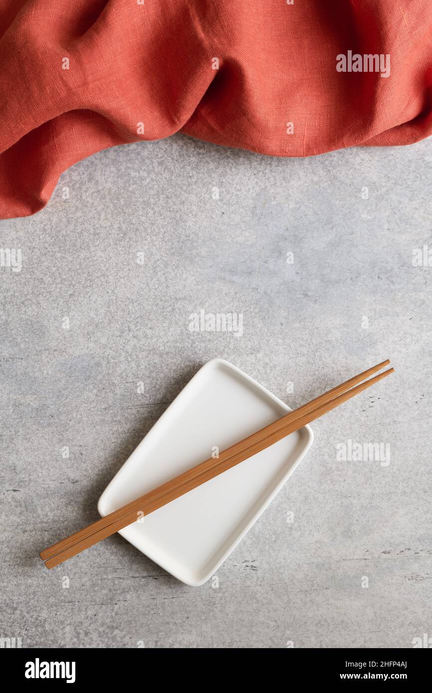Terrakotta-Serviette und leerer rechteckiger Teller mit Bambusstäbchen auf Betongrund mit Kopierfläche Stockfoto