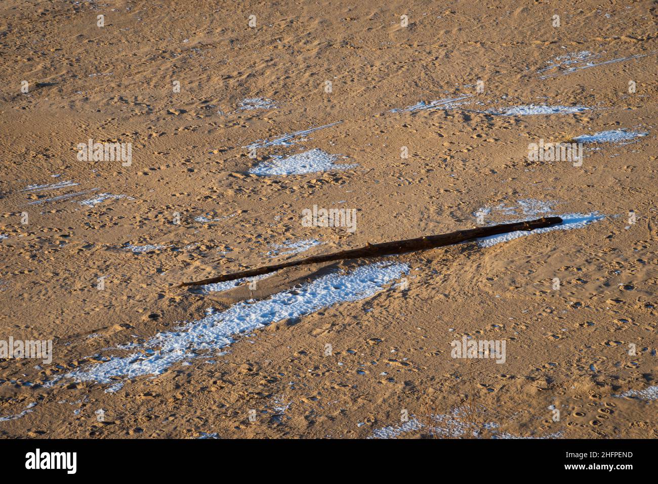 Sand am Strand im Winter mit etwas Schnee. Ein zerbrochener Holzpfahl am Meer ist abgebrochen. Stockfoto