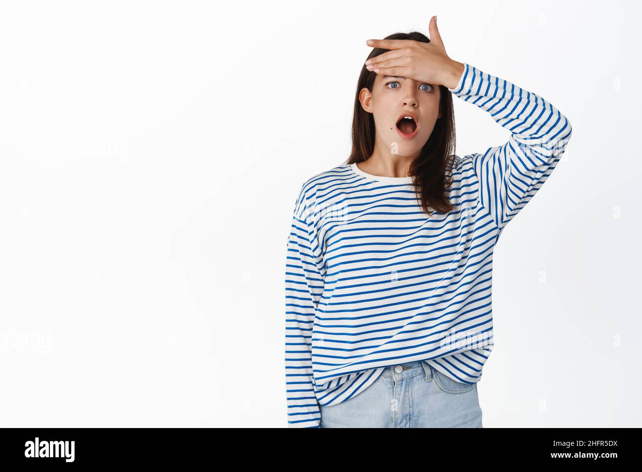 Schockiert Mädchen Student facepalm, starrte auf Kamera mit heruntergefallendem Kiefer, schlagen Stirn, vergessen erinnern smth, stand über weißem Hintergrund Stockfoto