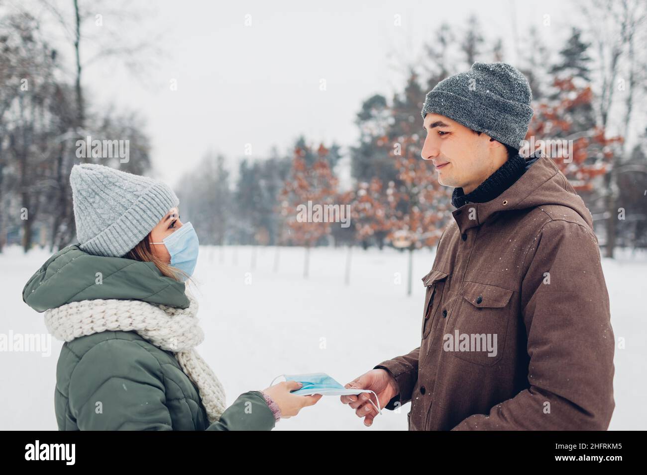 Frau gibt dem Freund im verschneiten Winterpark Maske. Paar gehen im Freien. Coronavirus kovid pandemische Sicherheitsmaßnahmen Stockfoto