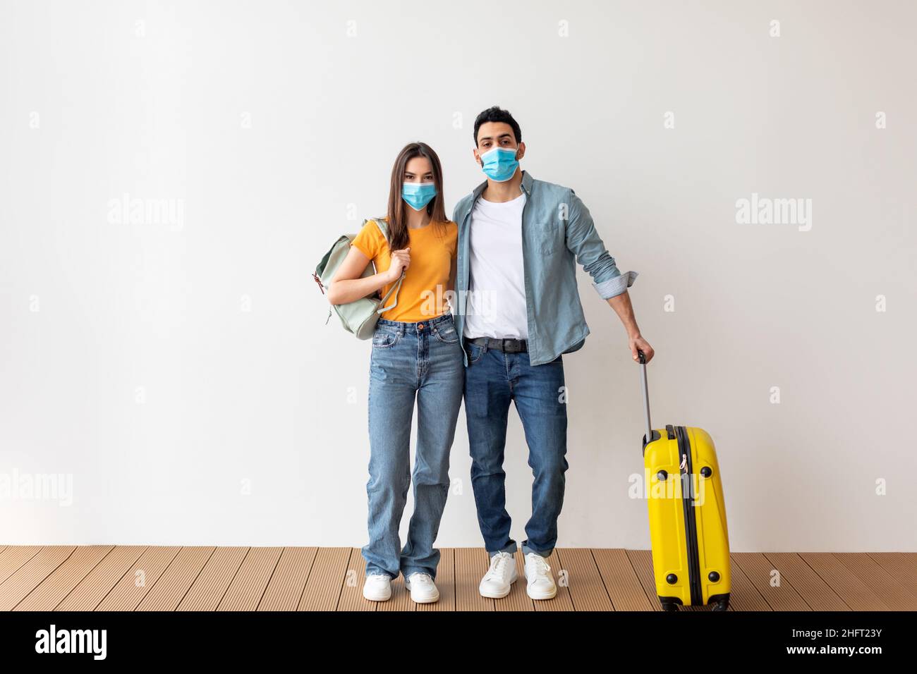 Coronavirus und Tourismus. Junges Paar in medizinischen Masken bereit für den Urlaub während der Pandemie, mit Gepäck stehen Stockfoto