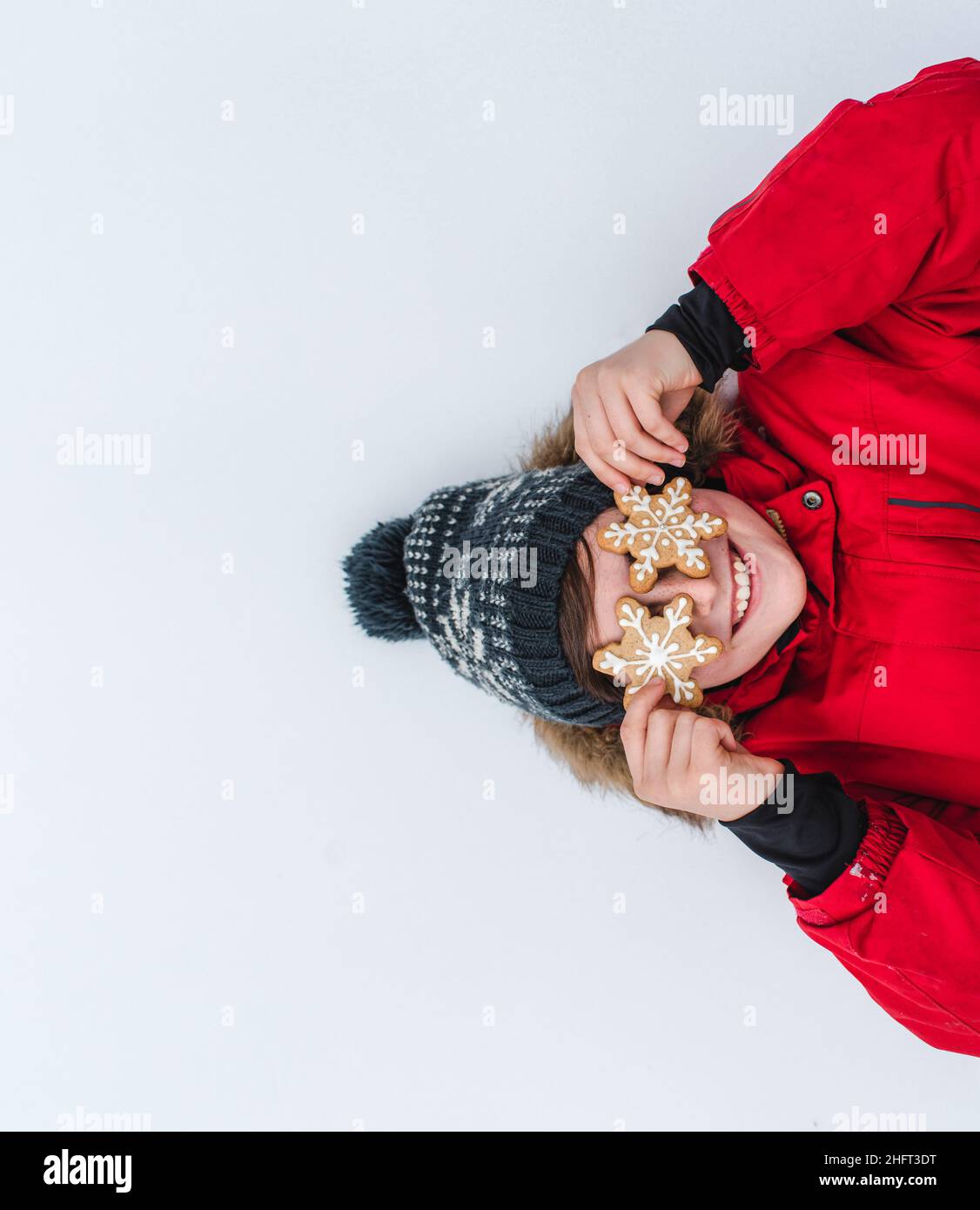 Über dem Kopf eines Jungen mit Schneeflockenkeksen über den Augen, die im Schnee liegen. Stockfoto