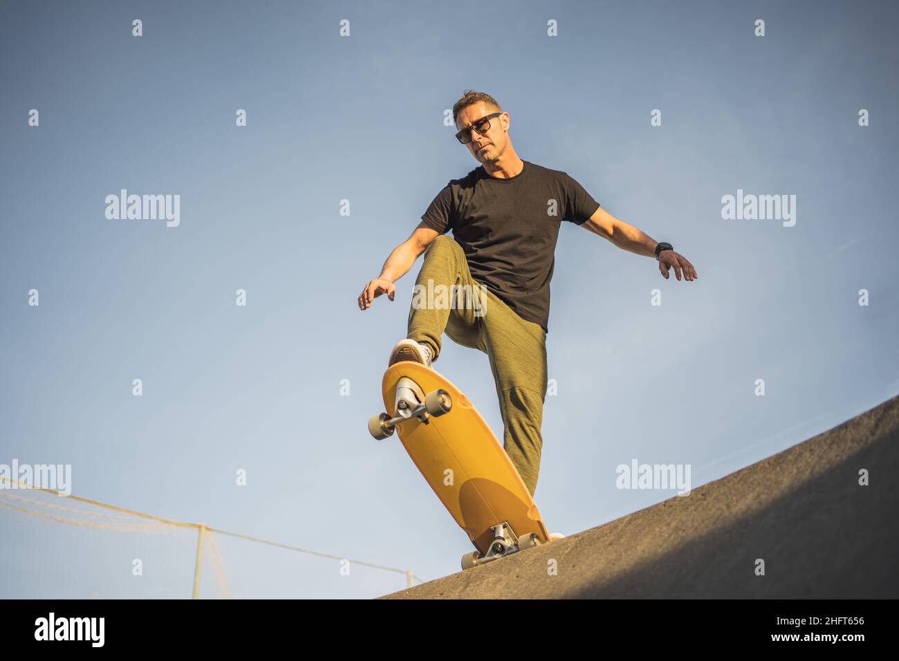 Ernsthafter erwachsener Mann bereitete sich darauf vor, mit Skate Surf auf einer Rampe nach unten zu gehen Stockfoto