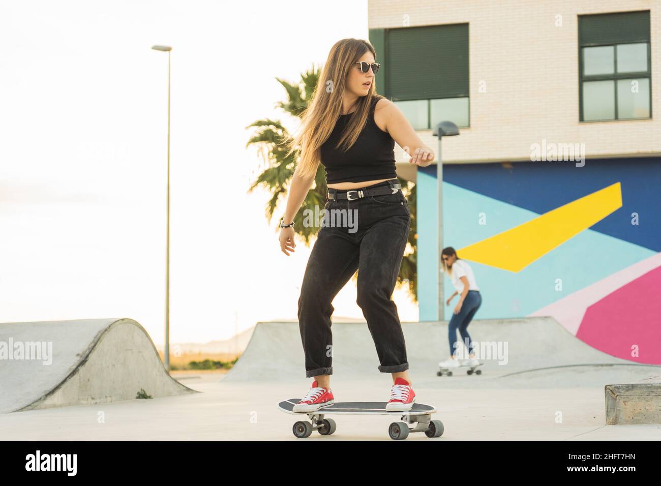 Junge Frau, die bei Sonnenuntergang im Park mit Surfskaten Schlittschuh laufen kann Stockfoto