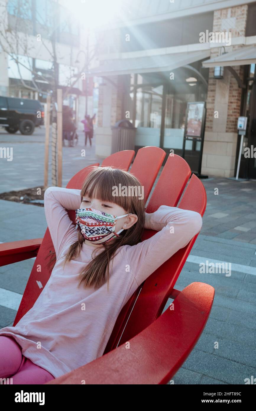 Junges Mädchen, das sich draußen mit Maske auf entspannt Stockfoto