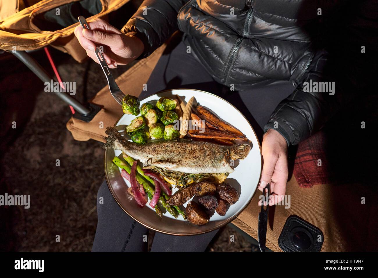 Die Frau hat ein Abendessen im Camp mit Forelle, rosenkohl und Karotten. Stockfoto