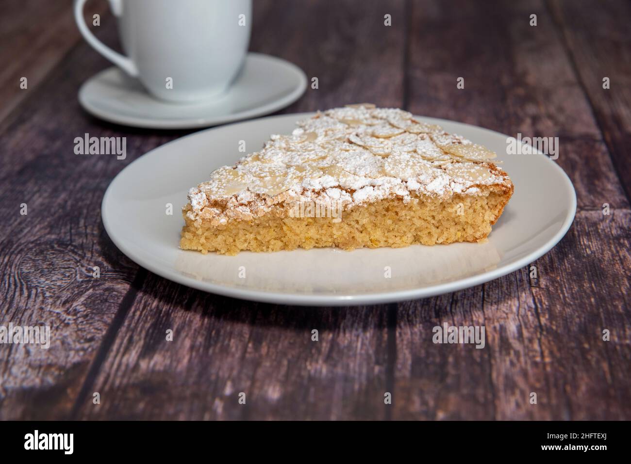 Ein Stück Mandelkuchen, serviert auf einem Holztisch mit Kaffee in einer Tasse Stockfoto