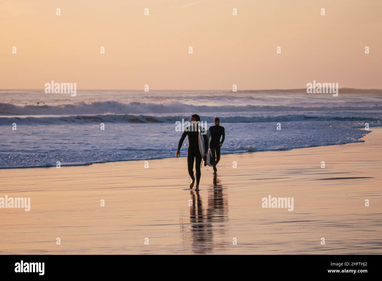 Zwei Surfer mit Surfbrett, die bei Sonnenuntergang an einem Strand surfen. Stockfoto