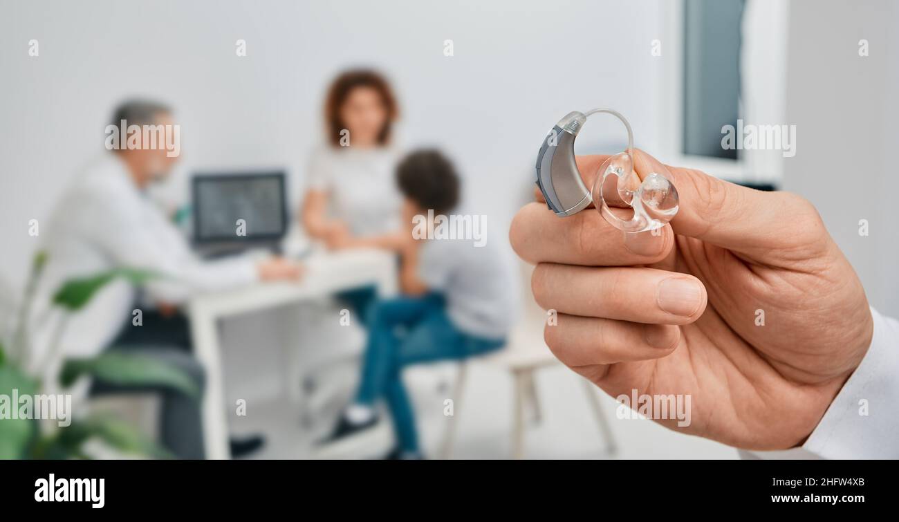 BTE-Hörgerät in den Händen des Arztes, Nahaufnahme. Auswahl von Hörgeräten für Kinderpatienten mit Audiologe über dem Hintergrund, weicher Fokus Stockfoto