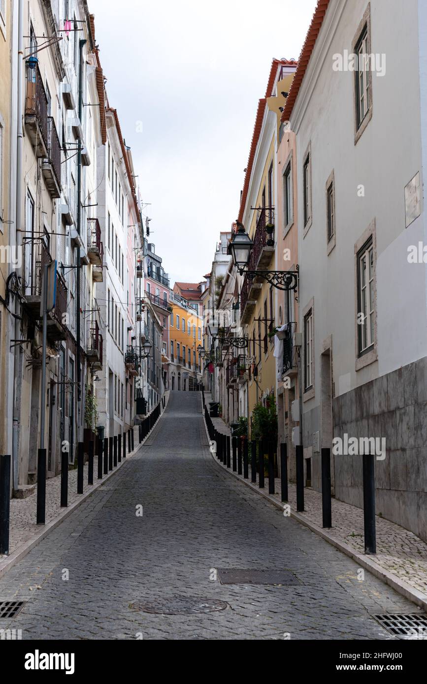 Kopfsteinpflasterstraße, die in eine hügelige Gegend führt, die an Wohngebäuden in Lissabon, Portugal, ausgerichtet ist Stockfoto