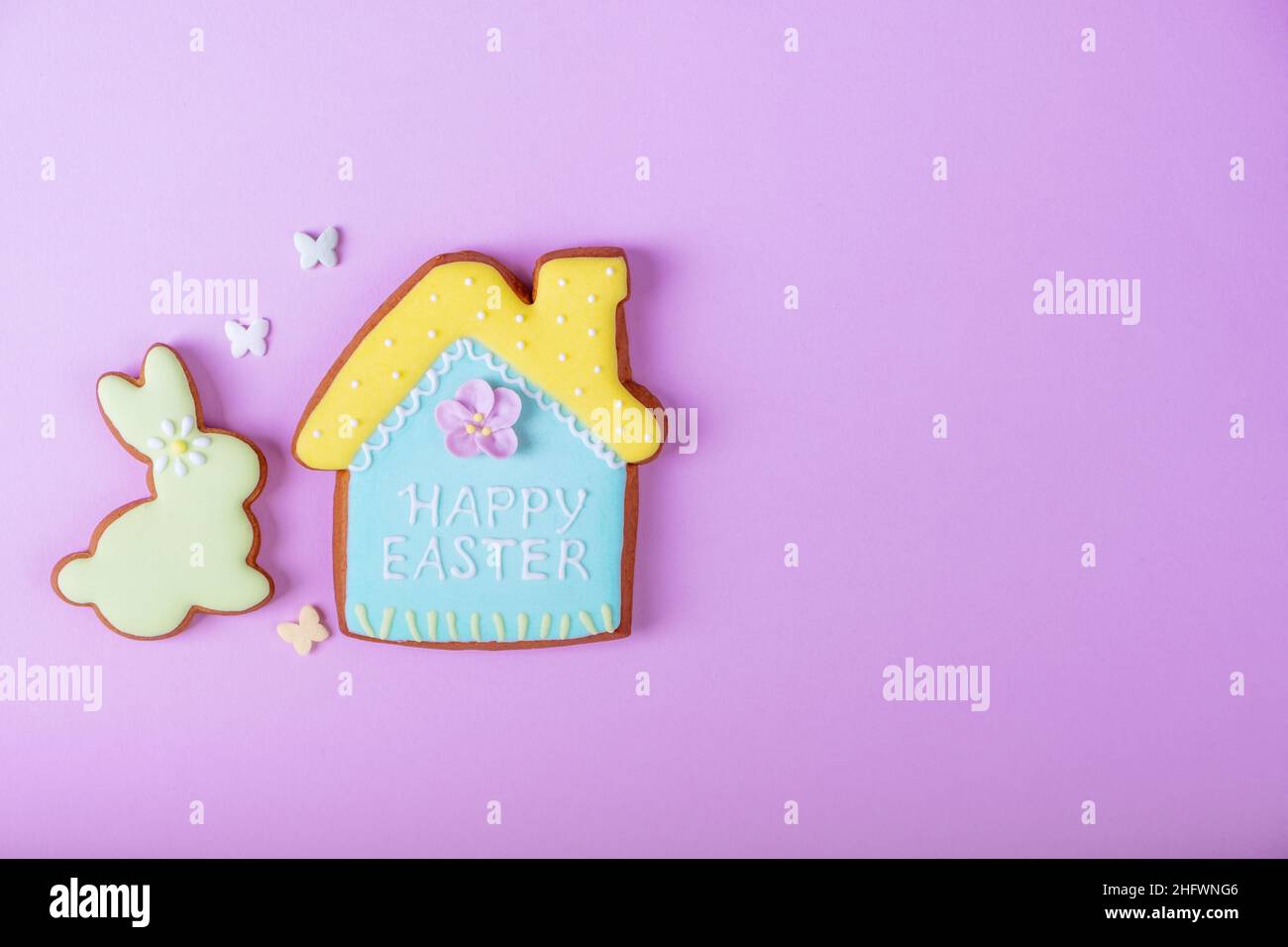 Frohe Ostern minimalistischer Hintergrund. Bunte Pastell-osterkekse auf violettem Hintergrund.Ostern Grußkarte mit buntem Kaninchen.Mock up. Banner. Draufsicht. Stockfoto