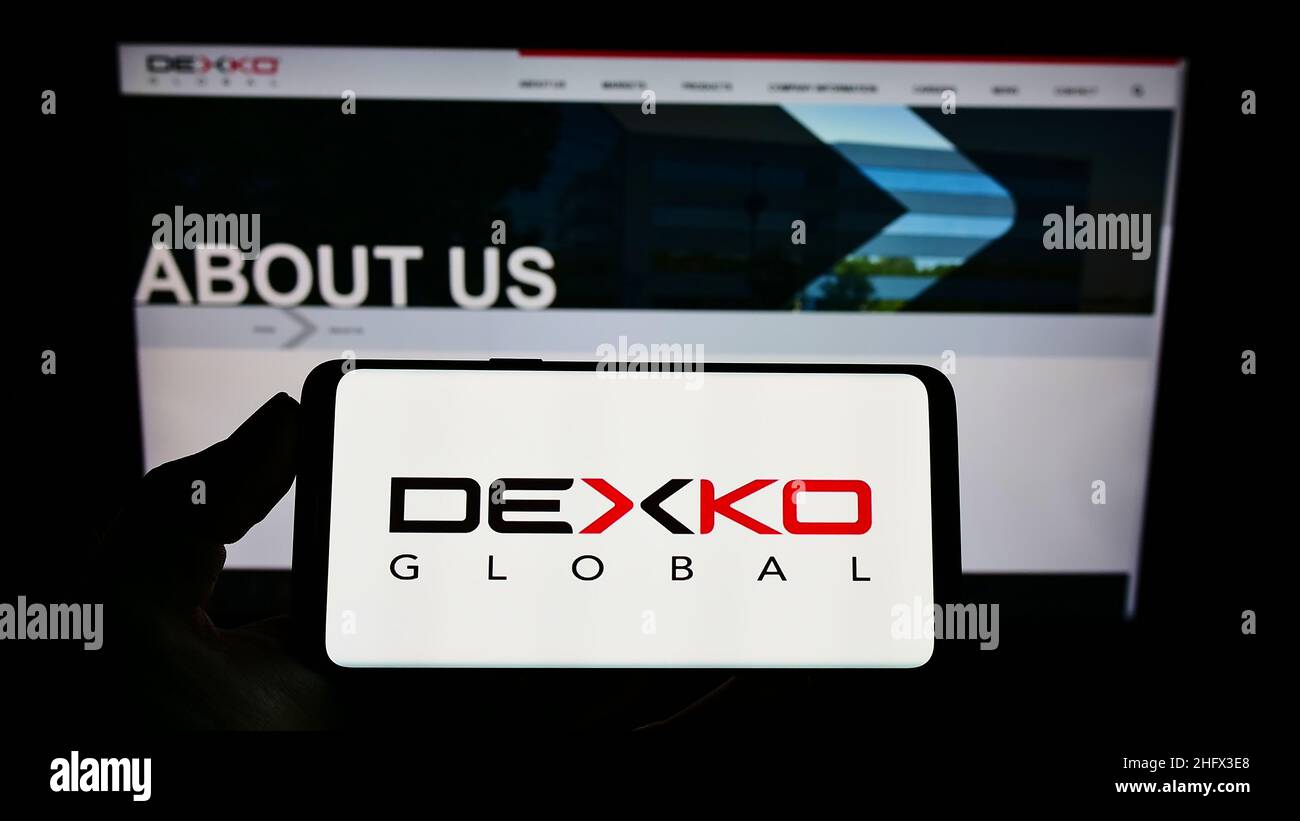 Person mit Mobiltelefon und Logo des amerikanischen Automobilunternehmens DexKo Global Inc. Auf dem Bildschirm vor der Webseite. Konzentrieren Sie sich auf die Telefonanzeige. Stockfoto