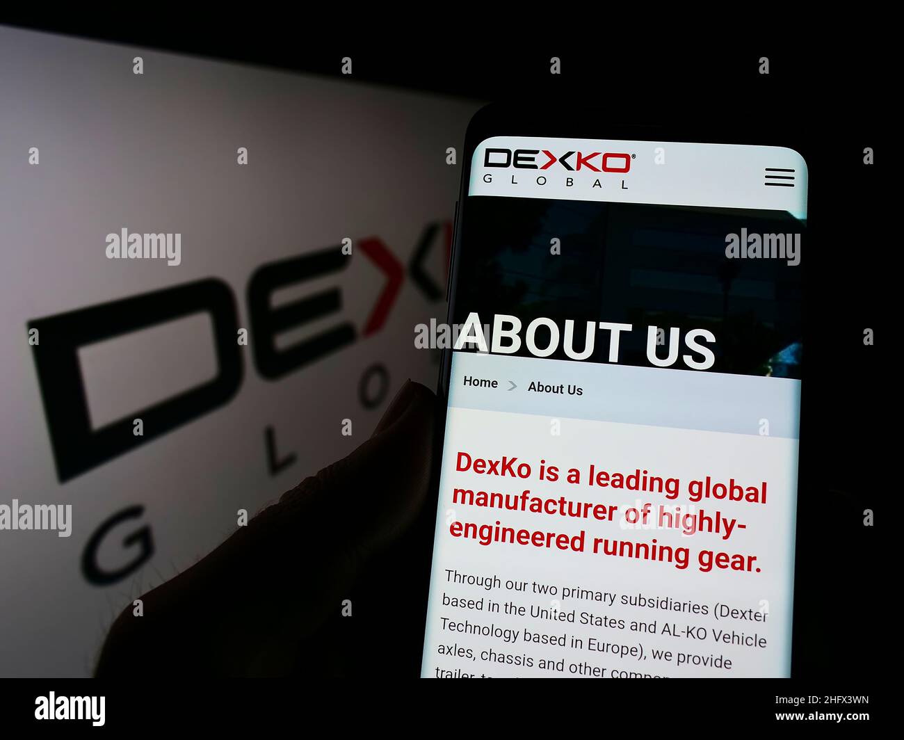 Person, die Mobiltelefon mit der Webseite des US-Automobilunternehmens DexKo Global Inc. Auf dem Bildschirm vor dem Logo hält. Konzentrieren Sie sich auf die Mitte des Telefondisplays. Stockfoto